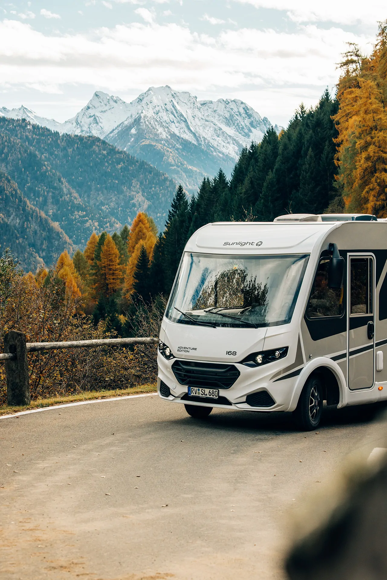 Ein Sunlight Wohnmobil fährt auf einer Bergstraße mit schneebedeckten Gipfeln im Hintergrund.