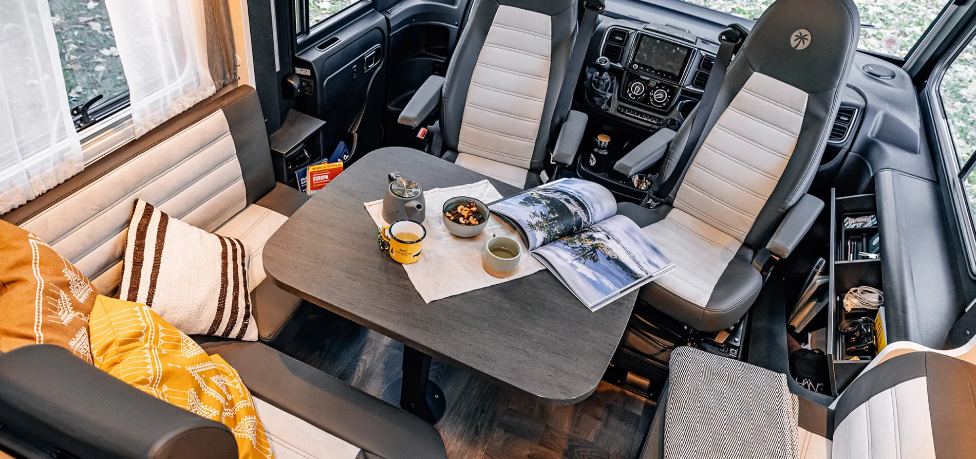 Innenraum eines Wohnmobils mit Tisch, vier Sitzen und einer Teekanne auf dem Tisch.