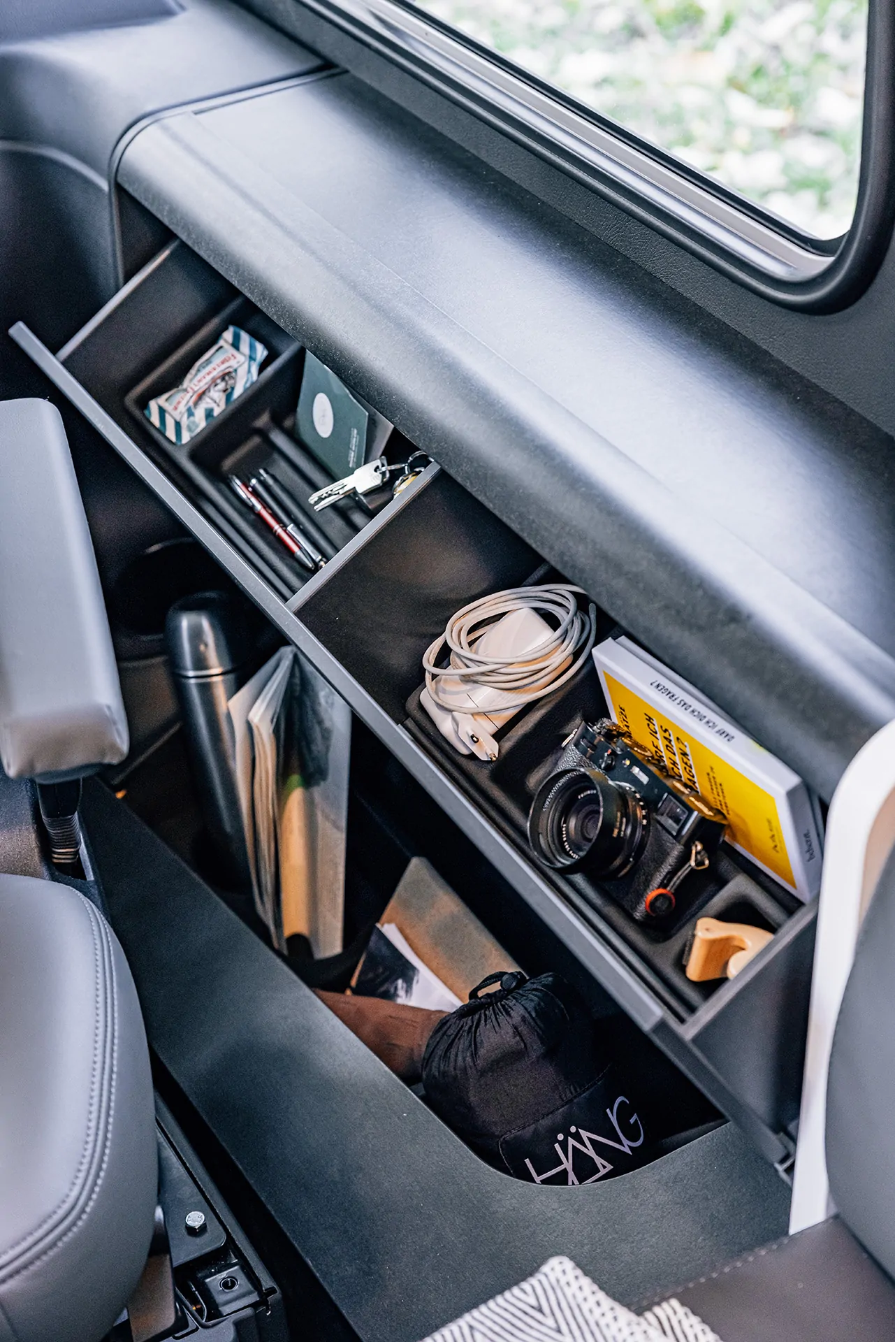 Ein Regal in einem Fahrzeug mit Kamera, Kabeln, Büchern und persönlichen Gegenständen.