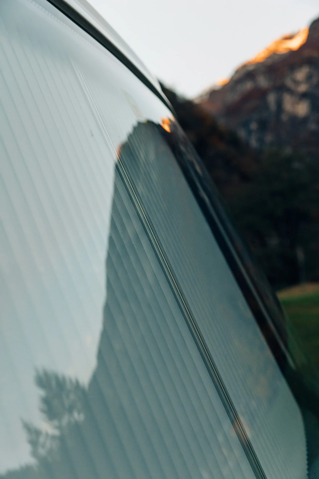 Nahaufnahme eines Fahrzeugs mit reflektiertem Bergpanorama im Fenster.