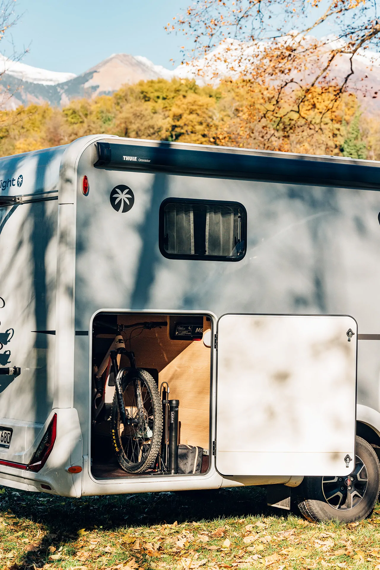 Ein Wohnmobil mit geöffneter Heckklappe zeigt ein verstautes Fahrrad, umgeben von herbstlicher Landschaft.