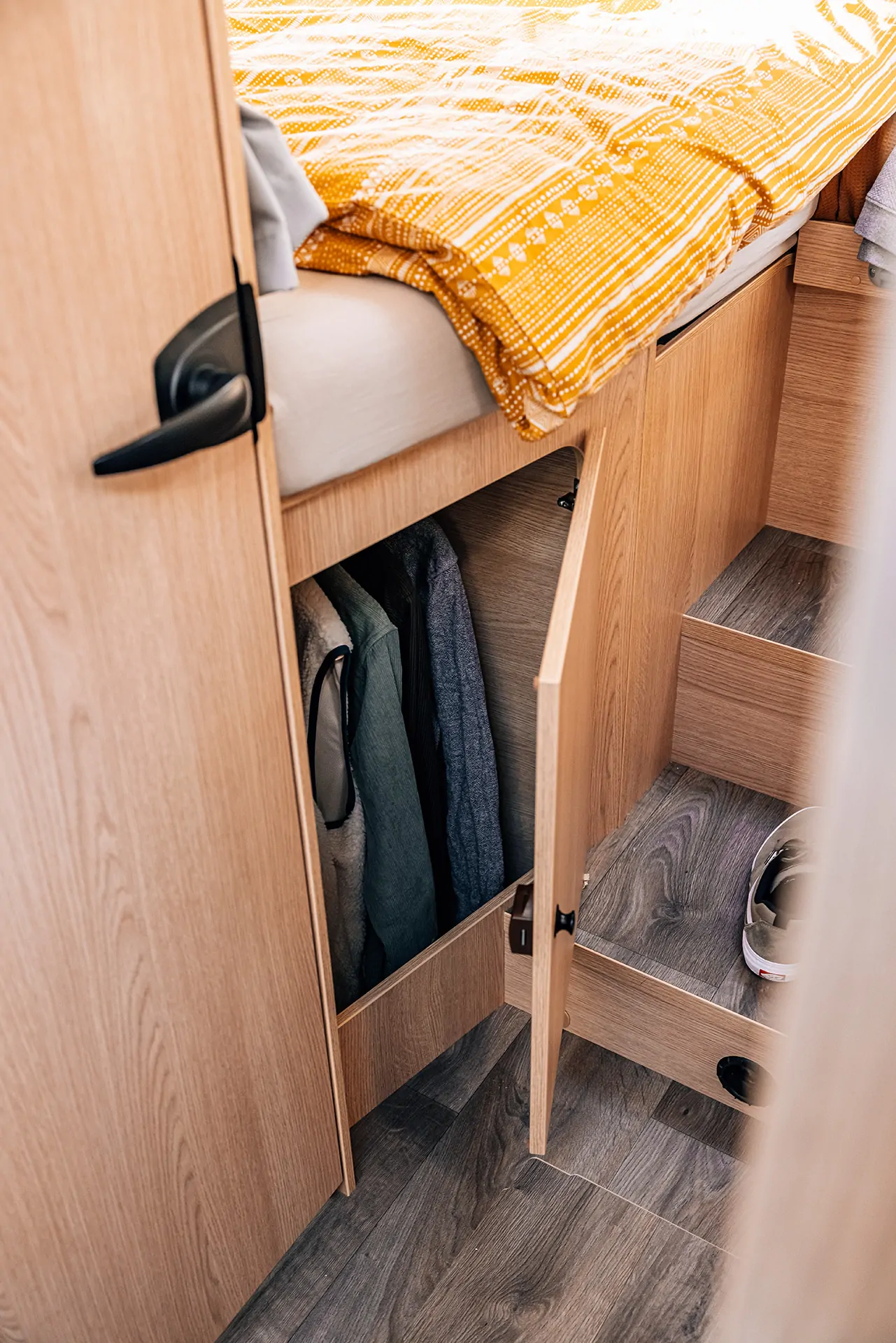 Ein geöffneter Schrank in einem Camper mit Kleidung und Schuhen sichtbar.