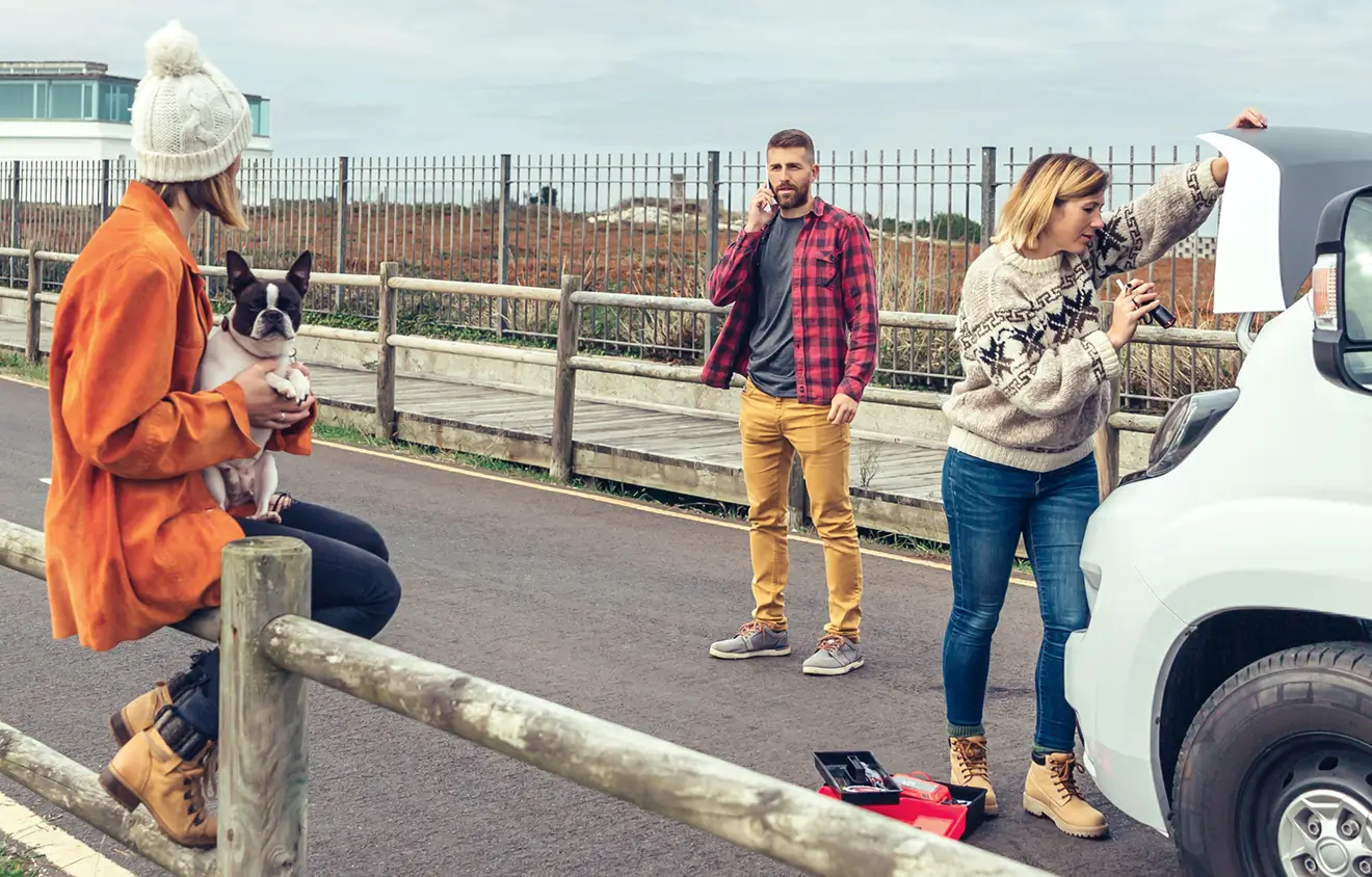 Personen mit Panne an einem Camper, eine ruft telefonierend um Hilfe.