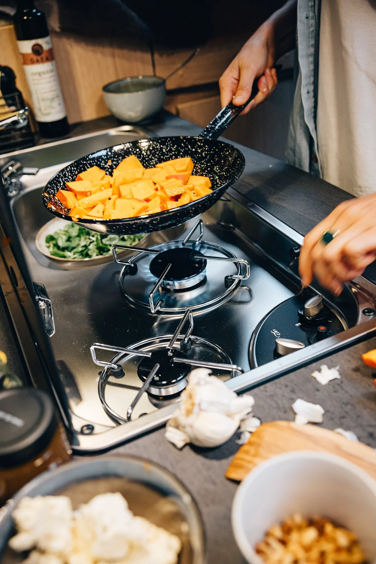 Eine Person kocht Kürbisstücke in einer Pfanne auf einem Gasherd.