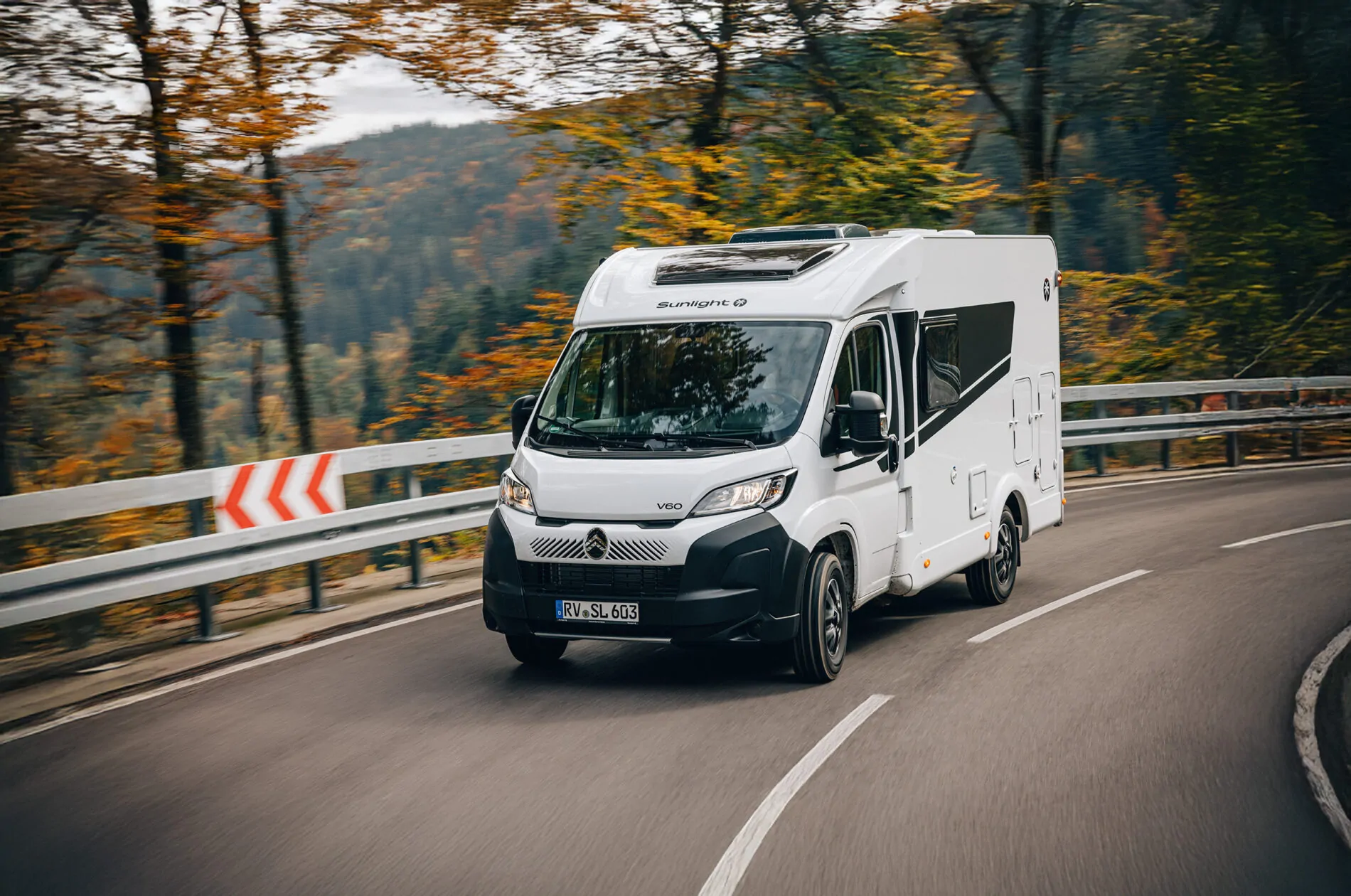 Wohnmobil Sunlight V60 fährt auf einer kurvigen Straße durch eine herbstliche Landschaft.