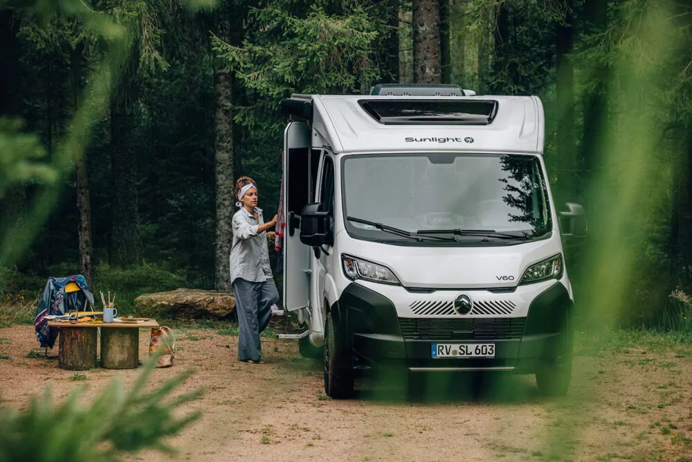 Eine Person steht neben einem Sunlight V60 Wohnmobil im Wald.