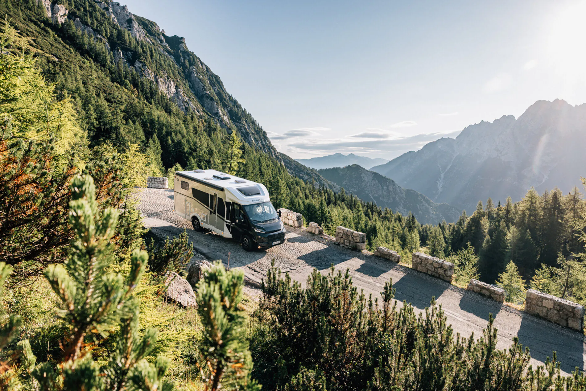 Ein teilintegriertes Wohnmobil fährt auf einer Bergstraße mit malerischem Ausblick.