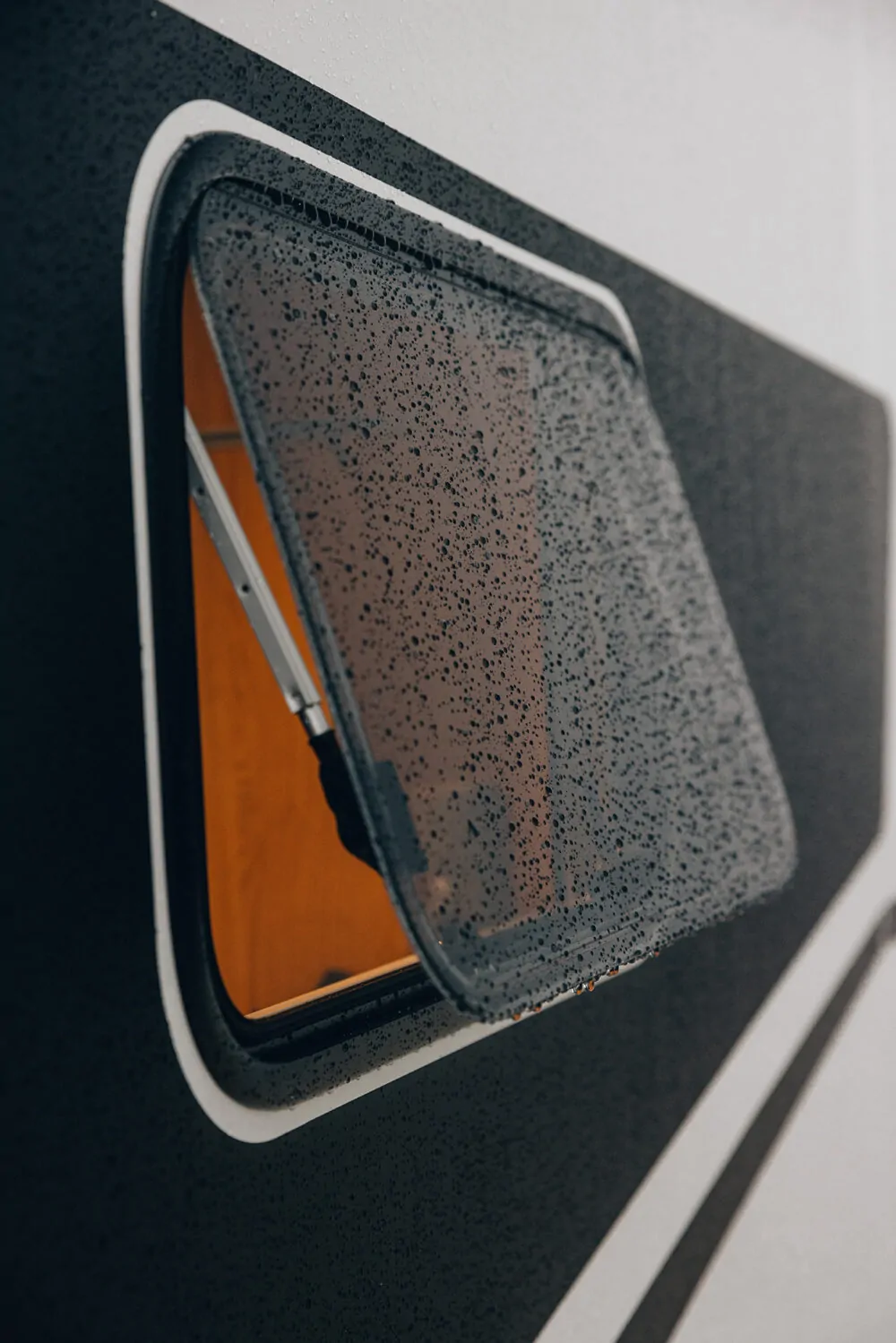 Ein geöffnetes, regennasses Fenster eines teilintegrierten Adventure-Campers.