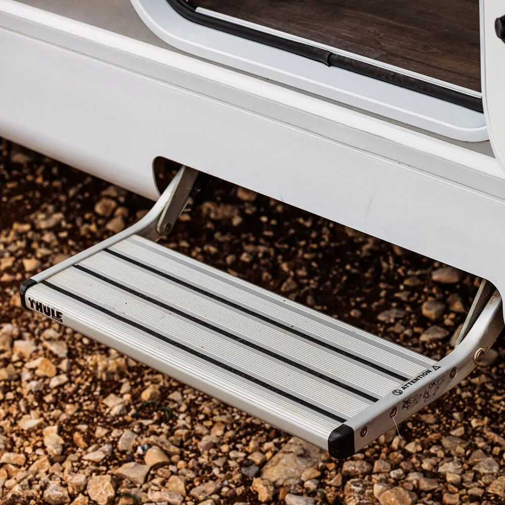 Ausziehbare Thule-Trittstufe an einem Wohnmobil auf steinigem Boden.