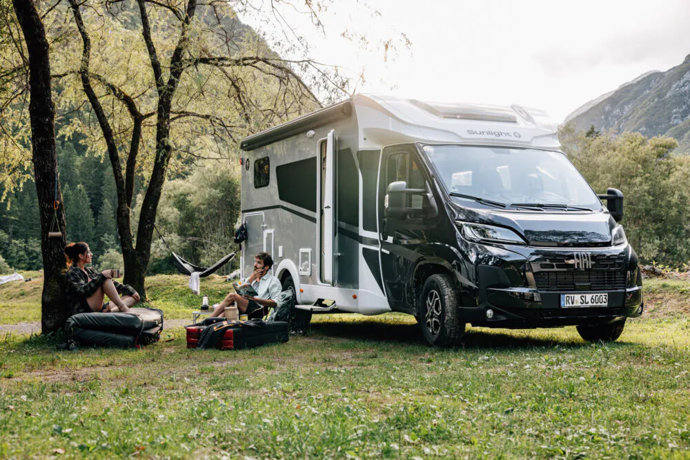 Zwei Personen sitzen vor einem Sunlight Wohnmobil in einer malerischen Waldlandschaft.