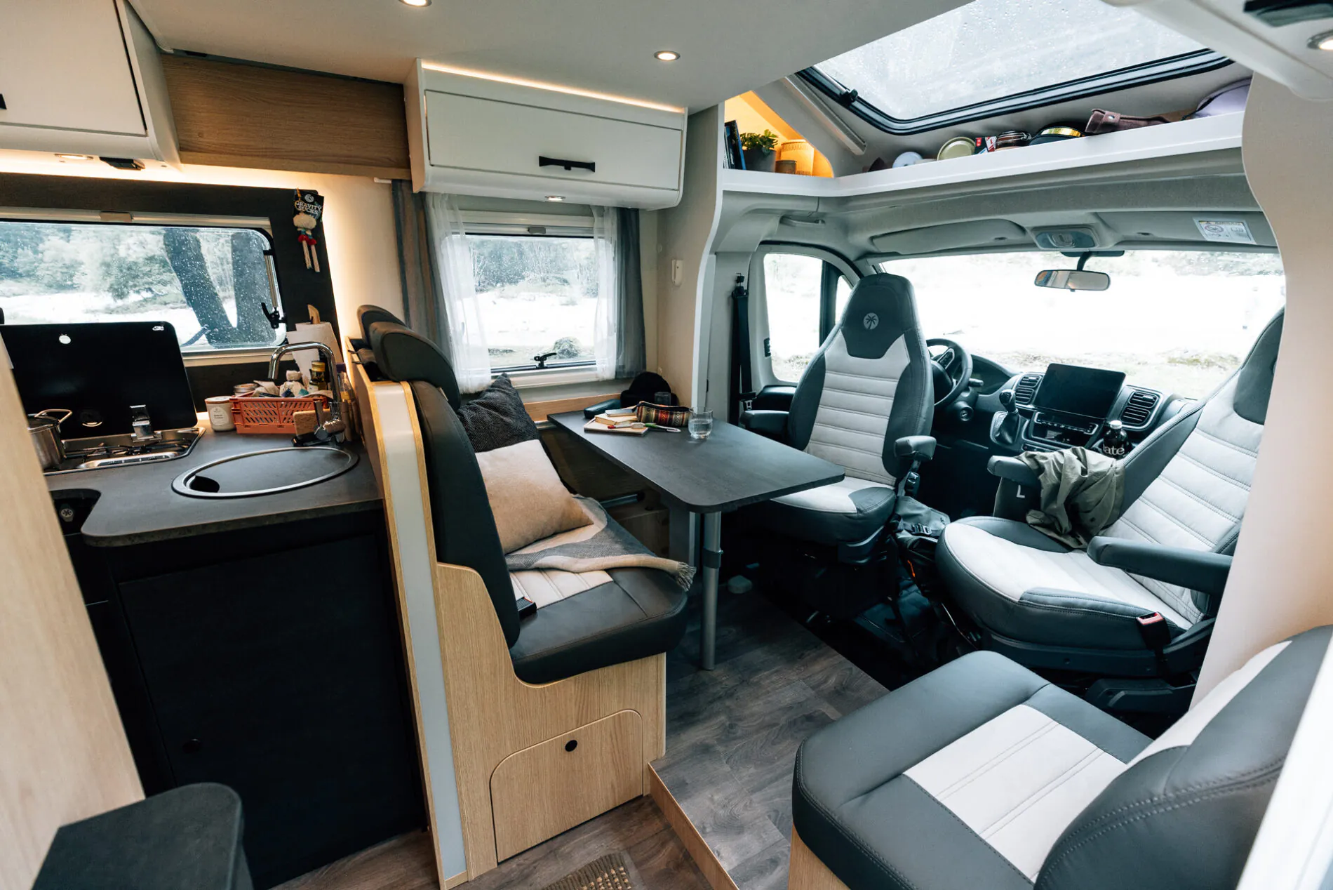 Innenansicht eines teilintegrierten Wohnmobils mit Sitzbereich, Tisch und Küchenzeile.