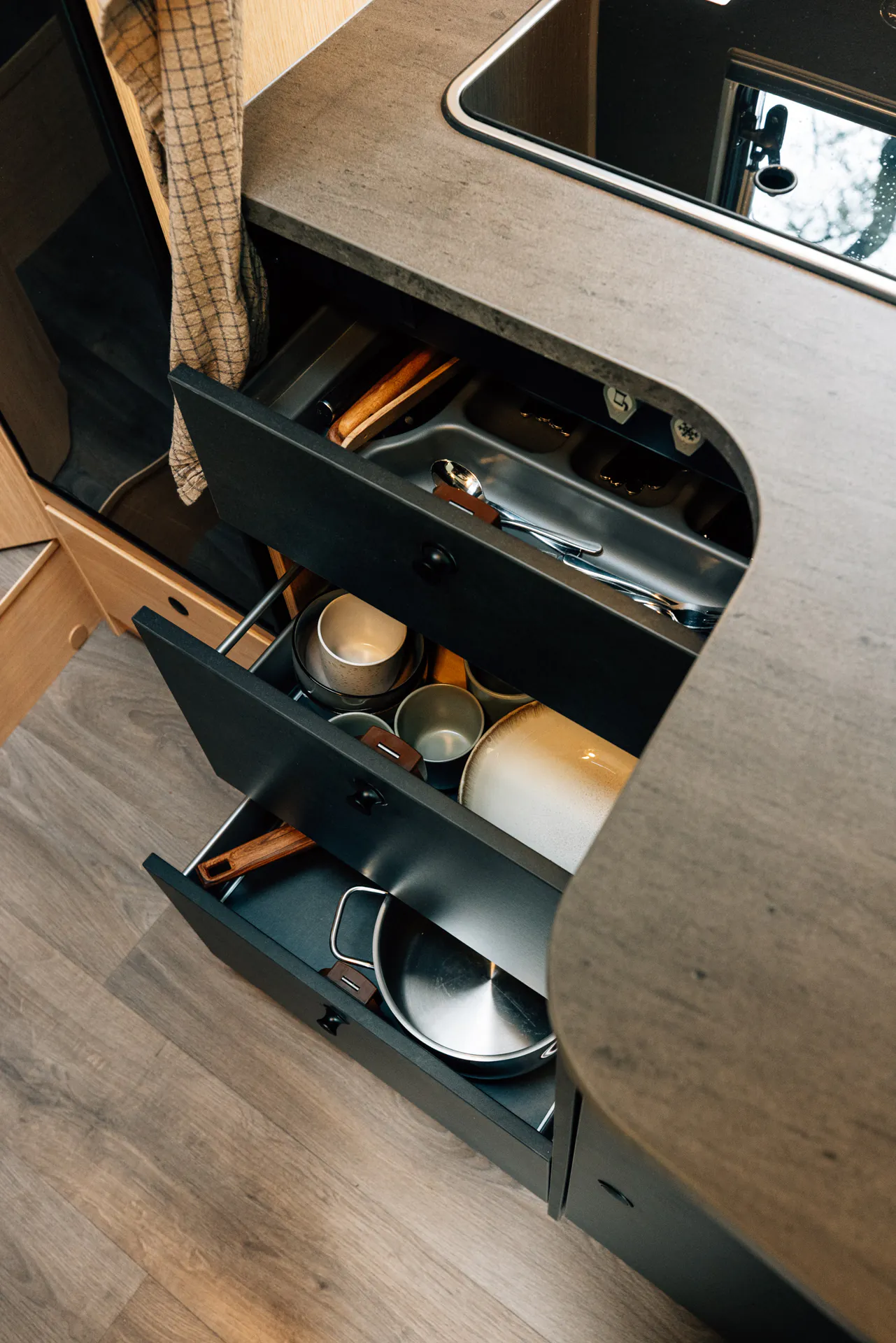 Offene Küchenschubladen in einem teilintegrierten Camper mit Geschirr und Besteck.