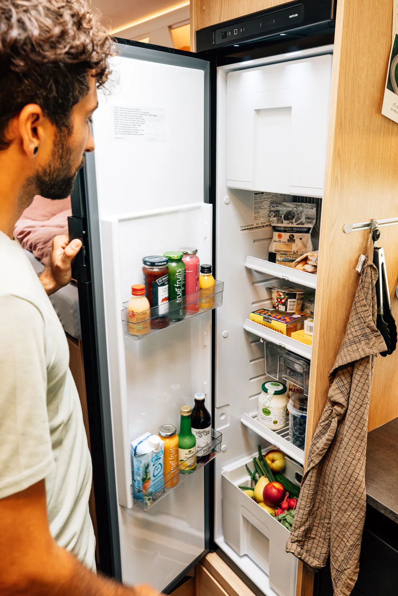 Eine Person öffnet den gut gefüllten Kühlschrank in einem Wohnmobil.