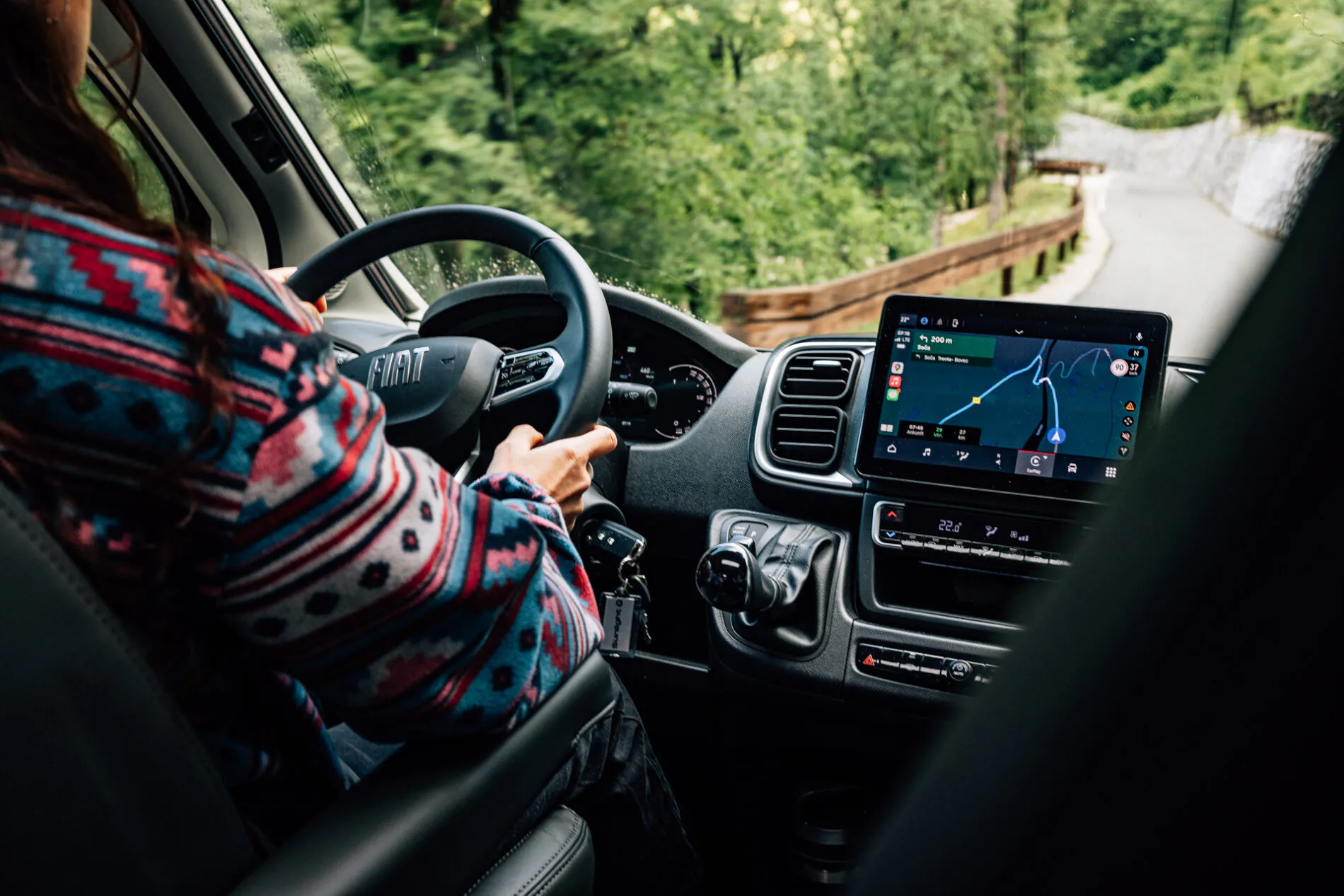 Person fährt einen Fiat mit einem Navigationssystem auf einer kurvigen Straße.