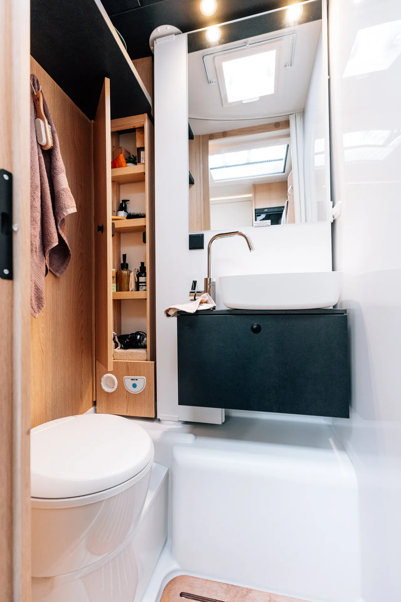 Innenansicht eines modernen Wohnmobil-Badezimmers mit Toilette, Waschbecken und Stauraum.