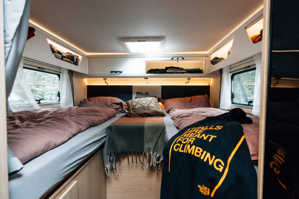 Innenansicht eines teilintegrierten Wohnmobils mit zwei Einzelbetten und modernen Beleuchtungselementen.
