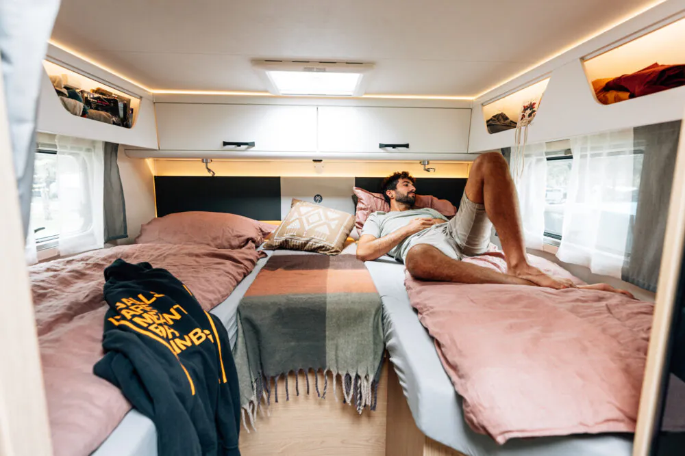 Ein Mann entspannt sich auf einem Bett in einem gemütlichen Wohnmobil-Interieur.