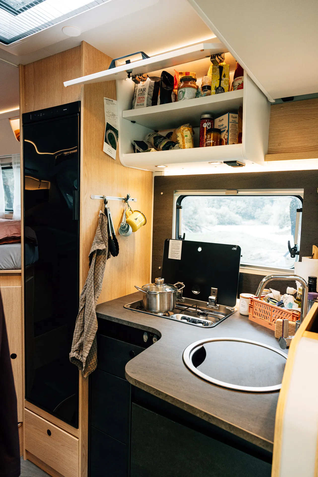 Kompakte Küche in einem teilintegrierten Adventure-Camper mit Herd, Spüle und offenem Schrank.