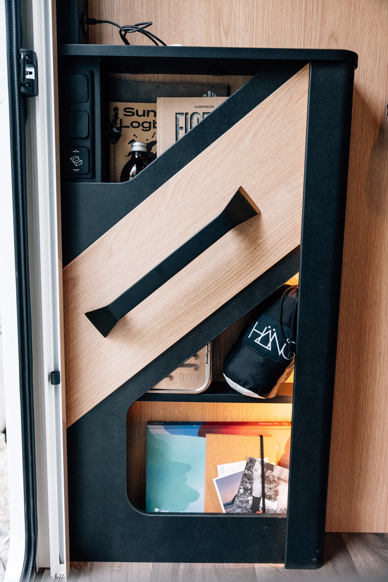 Innenraum eines Wohnmobils mit Regal, das Bücher, eine Flasche und andere Gegenstände enthält.