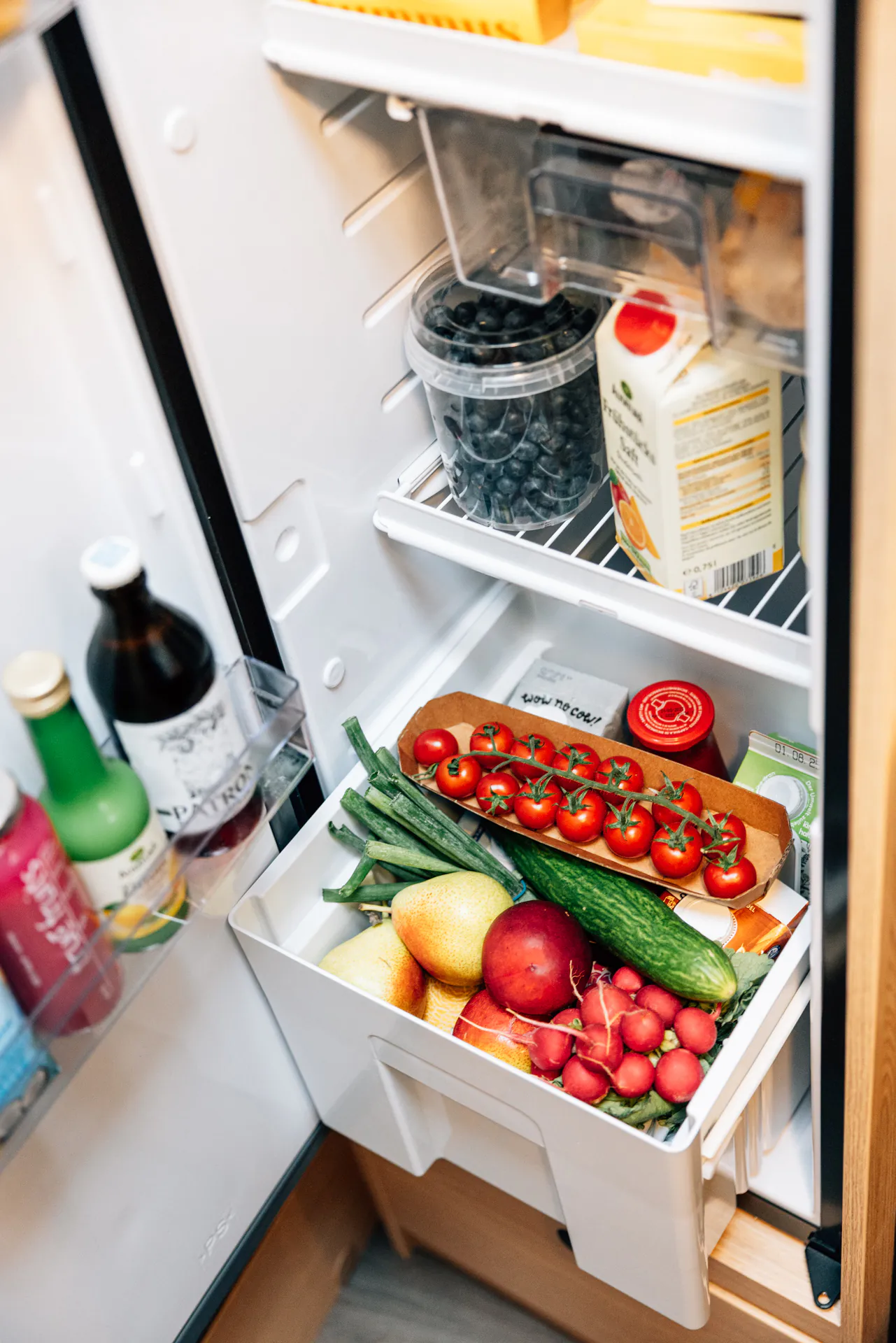 Ein geöffneter Kühlschrank mit frischem Obst, Gemüse und Getränken.