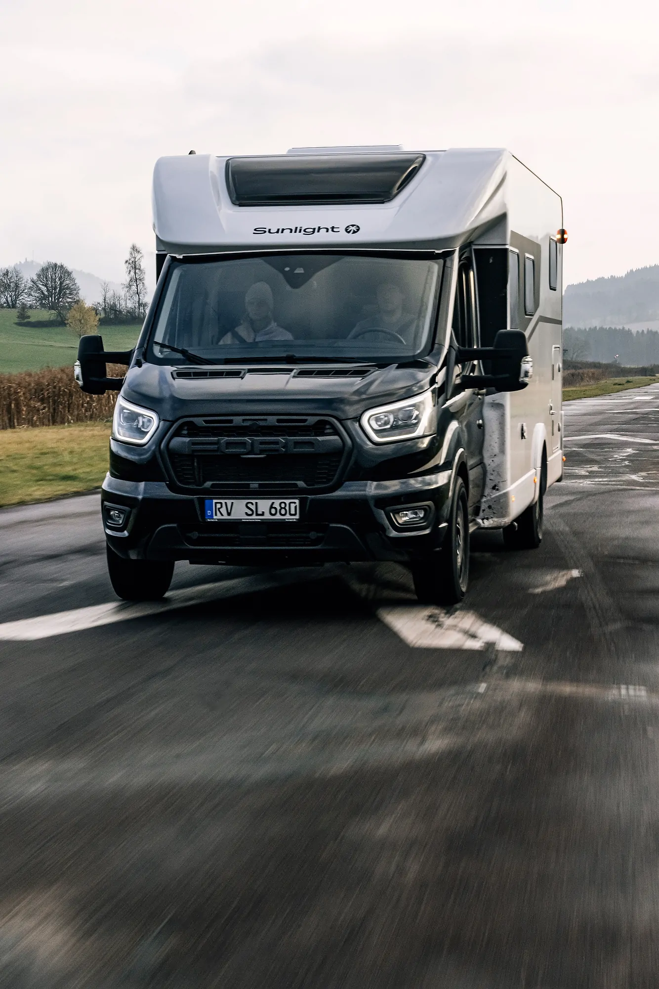 Teilintegriertes Wohnmobil Ford Adventure fährt auf einer Landstraße.
