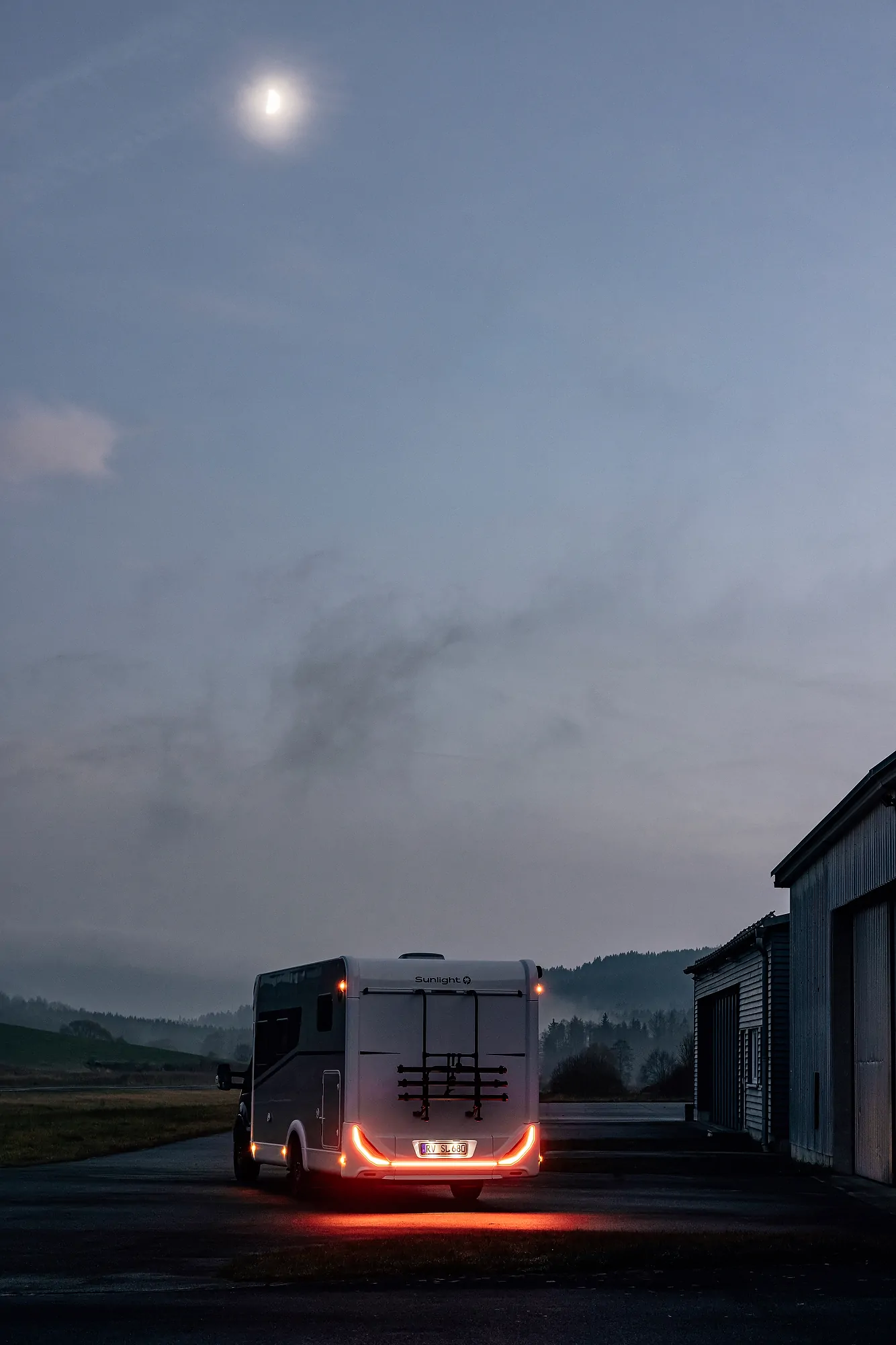 Wohnmobil bei Dämmerung auf einem Parkplatz mit eingeschaltetem Rücklicht.