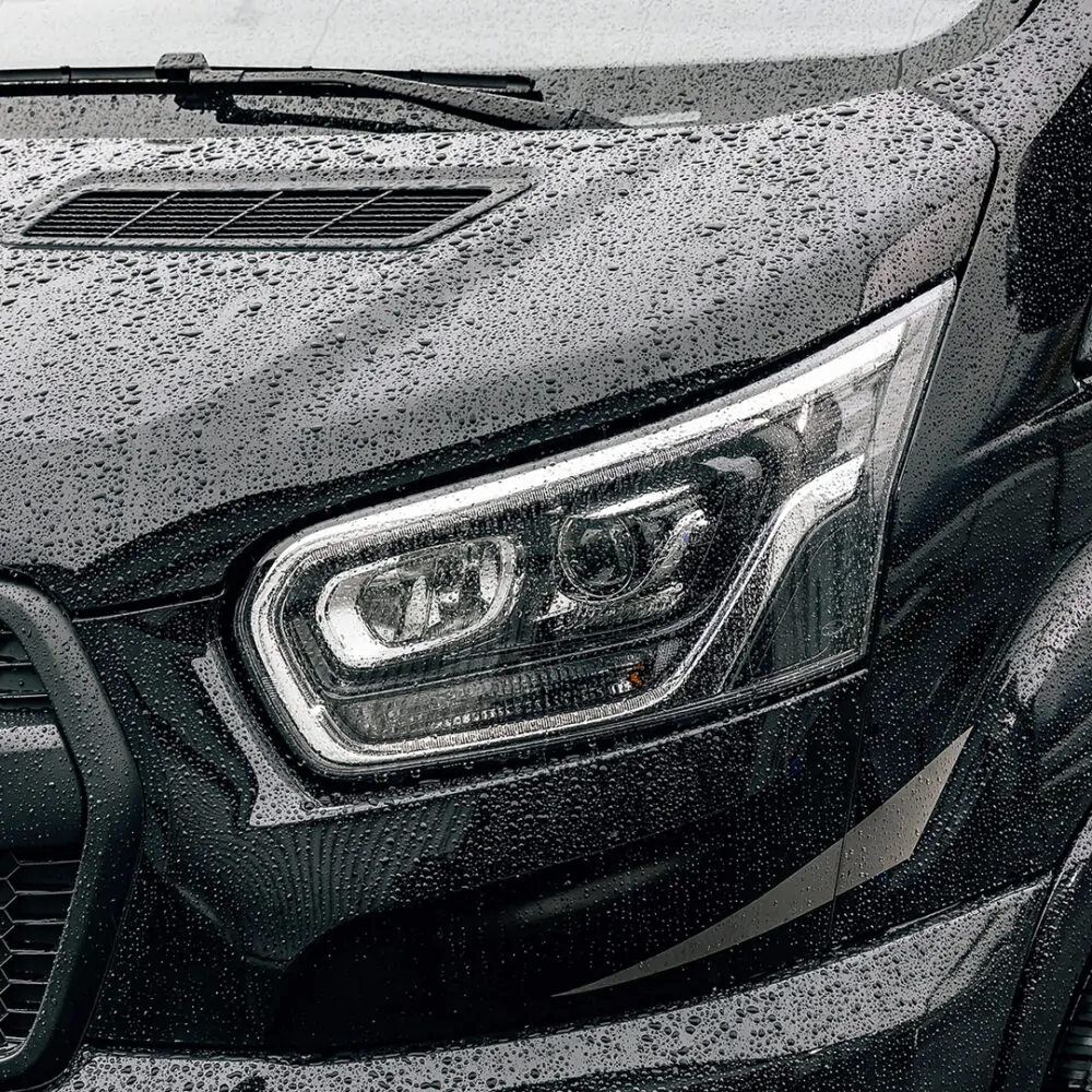 Nahaufnahme eines Scheinwerfers des Ford Adventure Wohnmobils mit Regentropfen auf der Oberfläche.