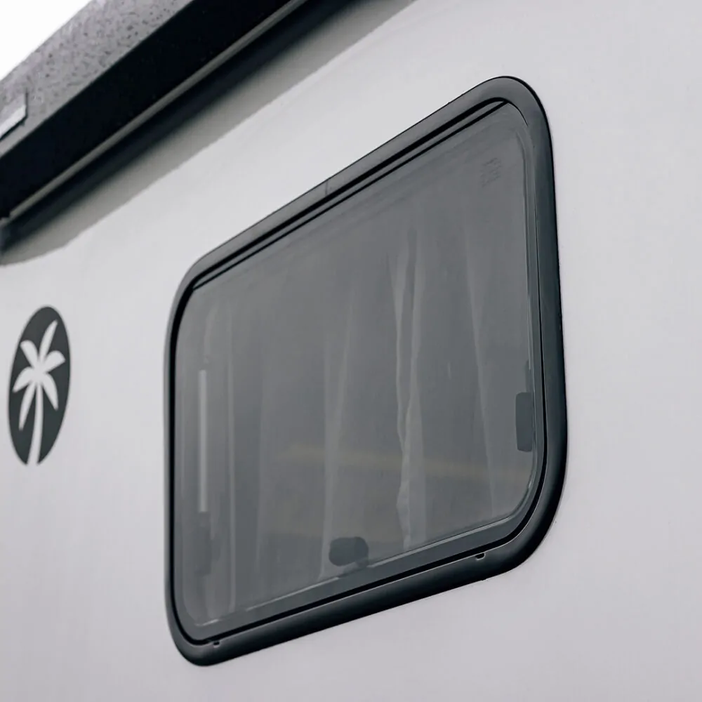 Fenster eines Ford Adventure Wohnmobils mit Palmen-Logo auf der Seite.