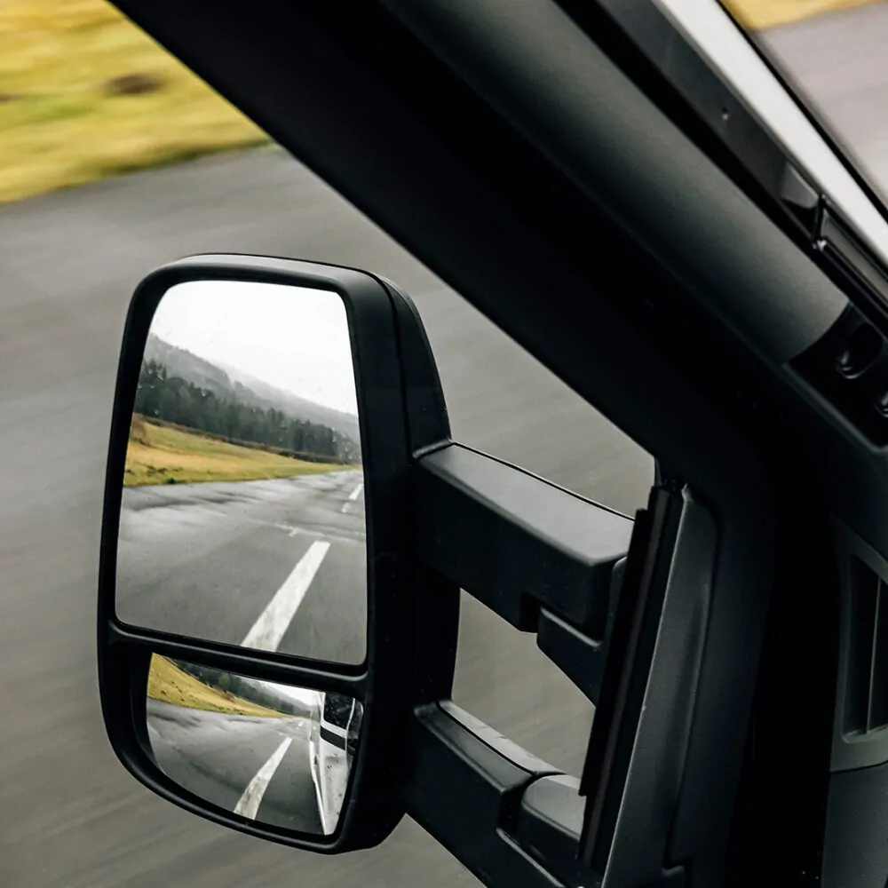 Seitenspiegel eines Fahrzeugs zeigt eine leere Landstraße.