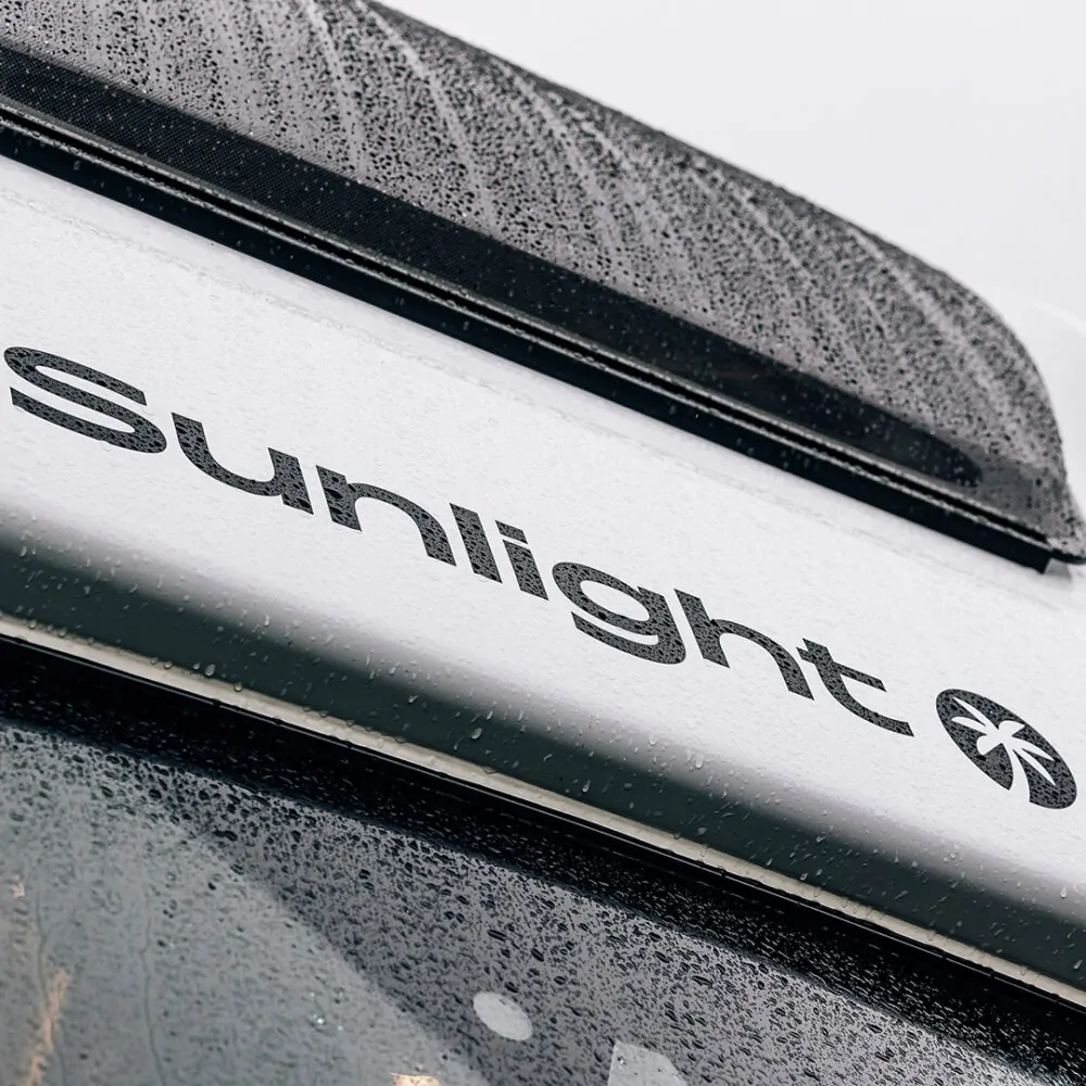 Nahaufnahme eines Wohnmobils mit dem Schriftzug "Sunlight" und Regentropfen auf der Oberfläche.