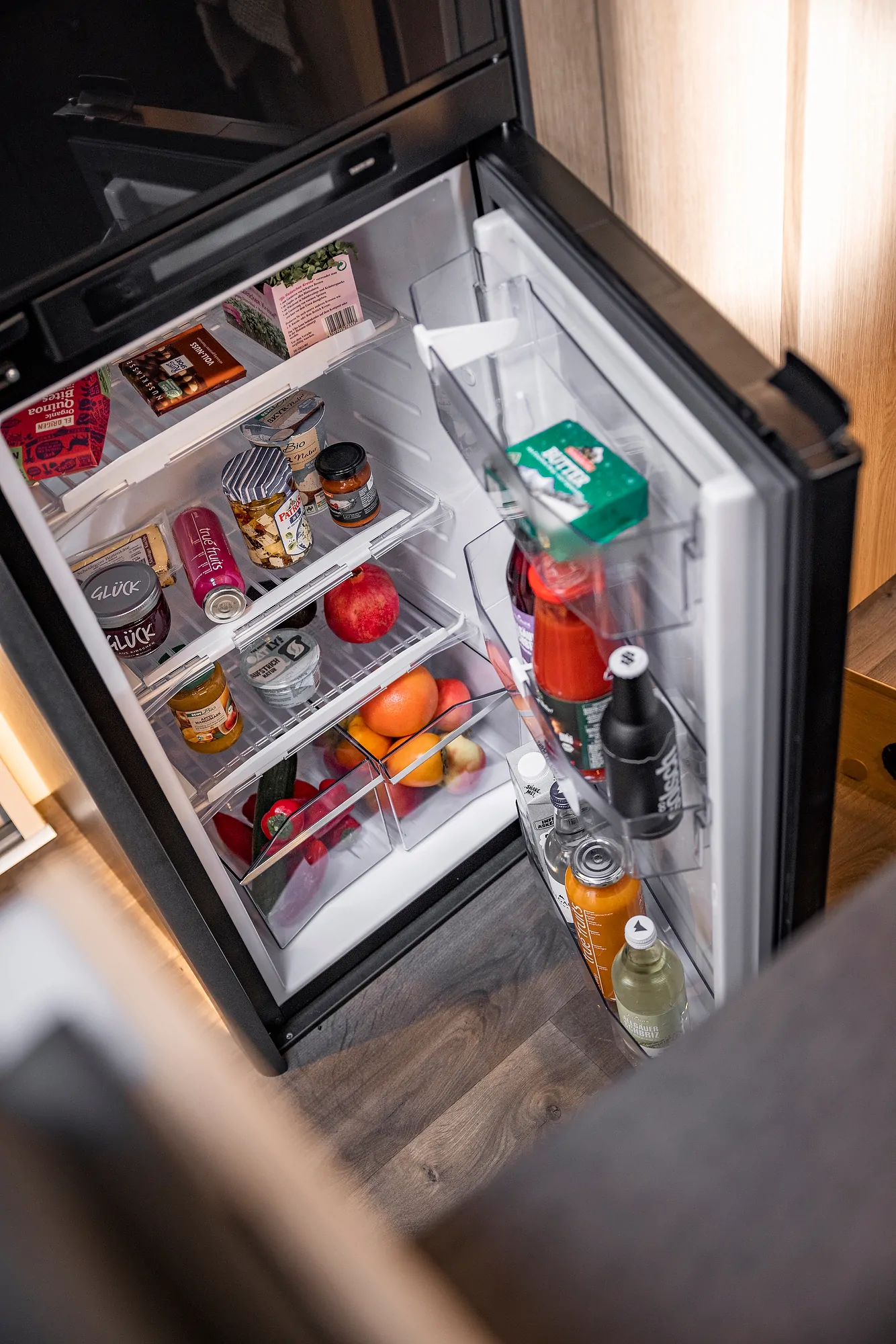 Ein geöffneter Kühlschrank in einem Ford Adventure Camper zeigt verschiedene Lebensmittel und Getränke.