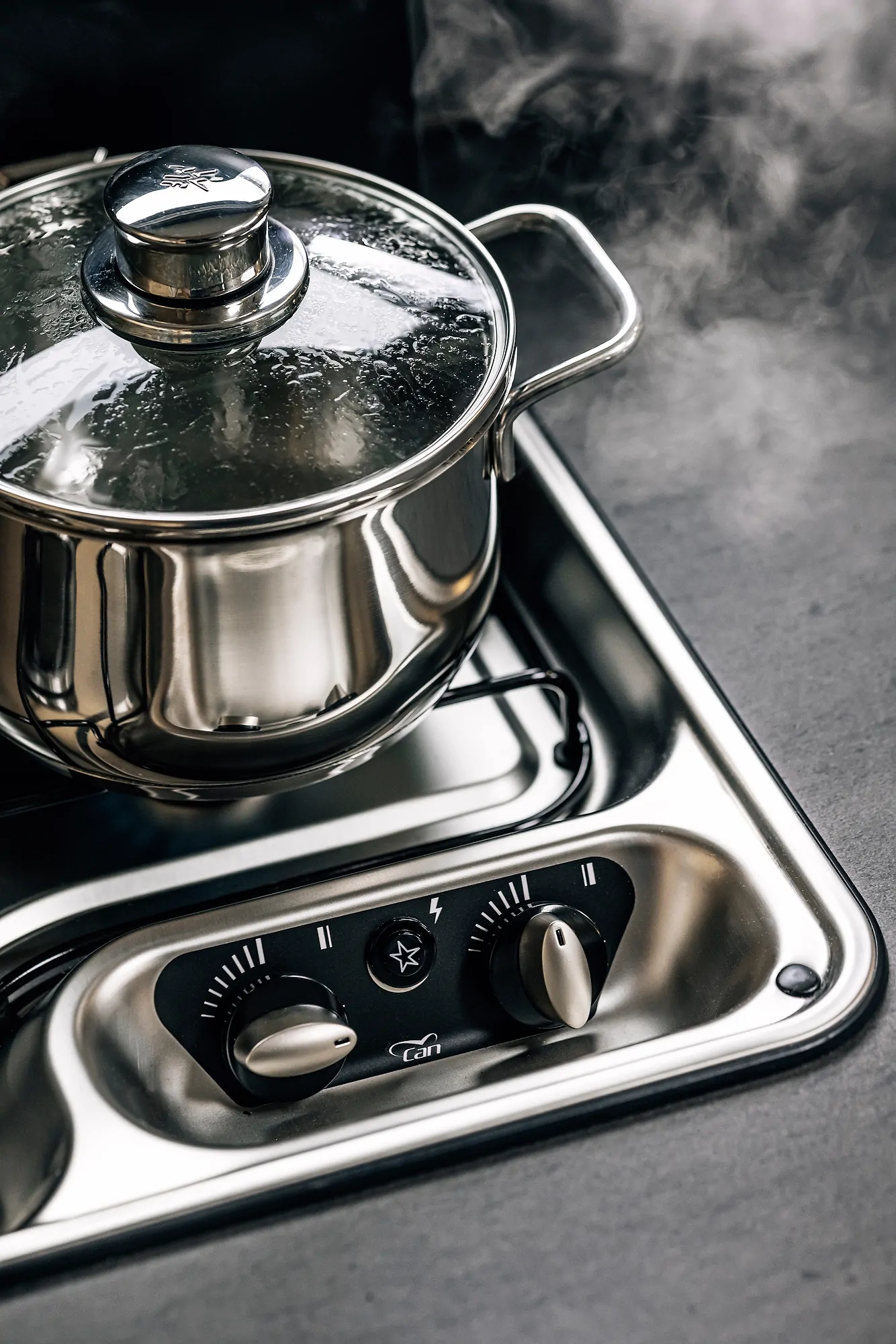 Ein dampfender Topf mit Deckel steht auf einem Herd mit Bedienelementen.