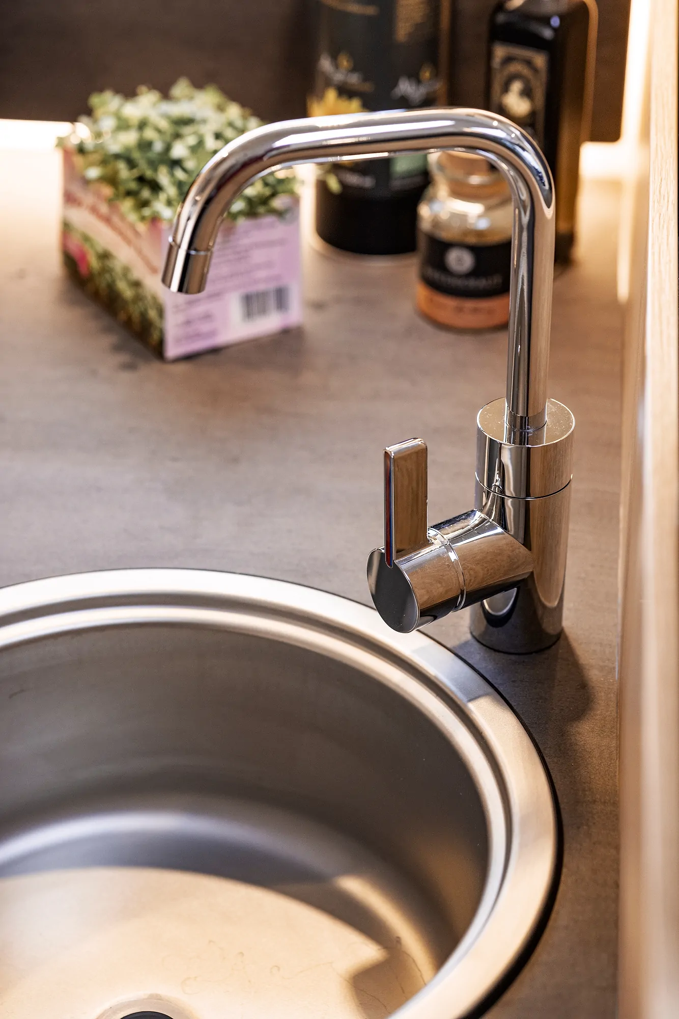 Küchenspüle mit glänzendem Wasserhahn und Kräutern im Hintergrund.
