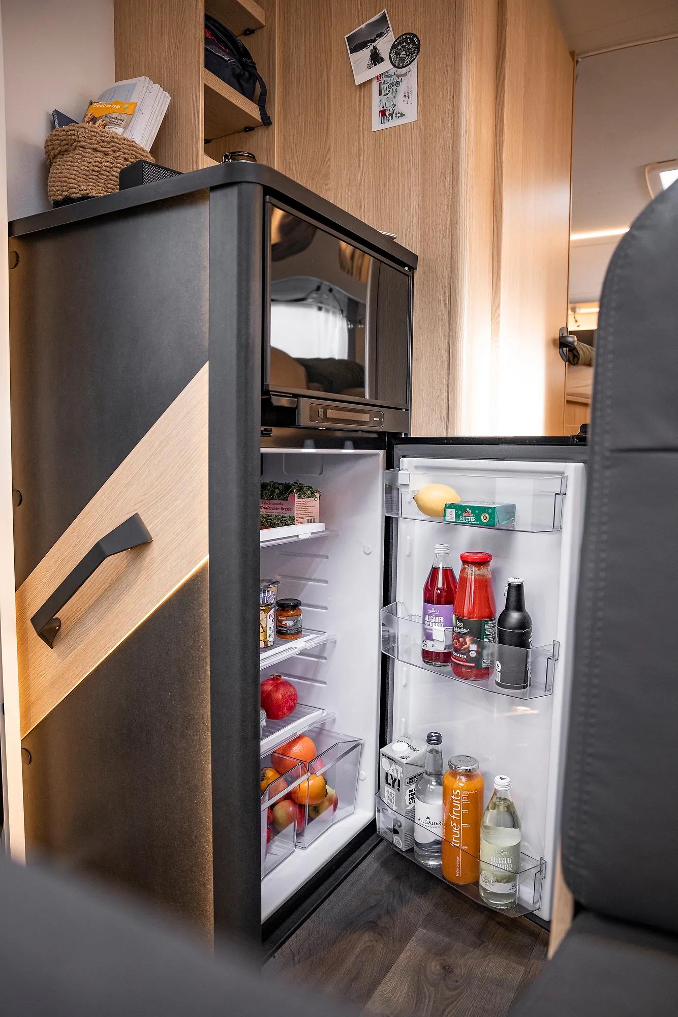 Ein geöffneter Kühlschrank in einem Ford Adventure Wohnmobil zeigt Getränke und Obst.