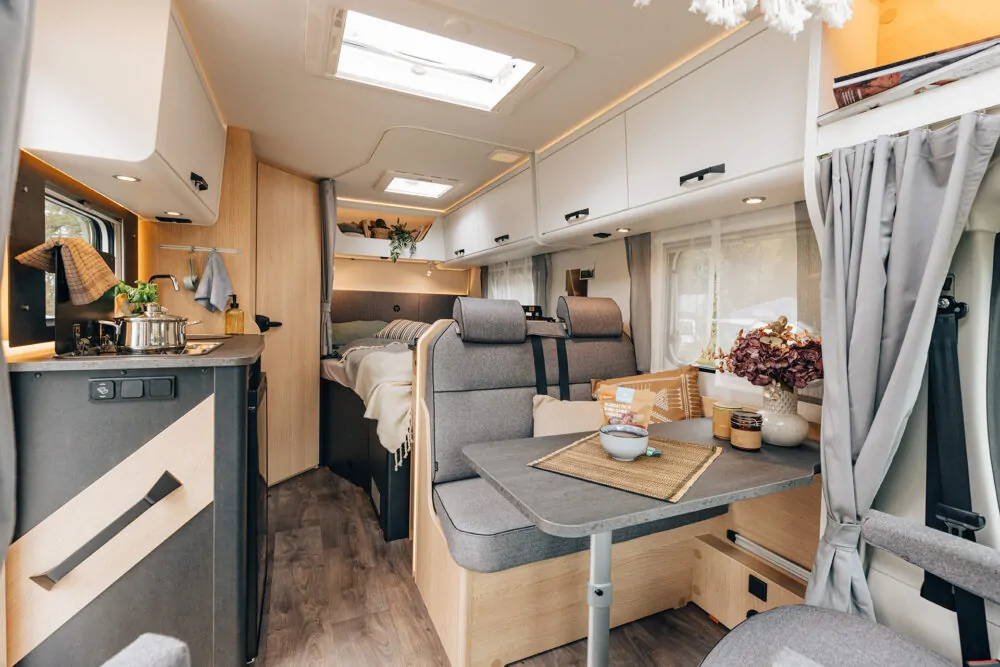 Innenraum eines teilintegrierten Wohnmobils mit moderner Küche, Esstisch und Schlafbereich.