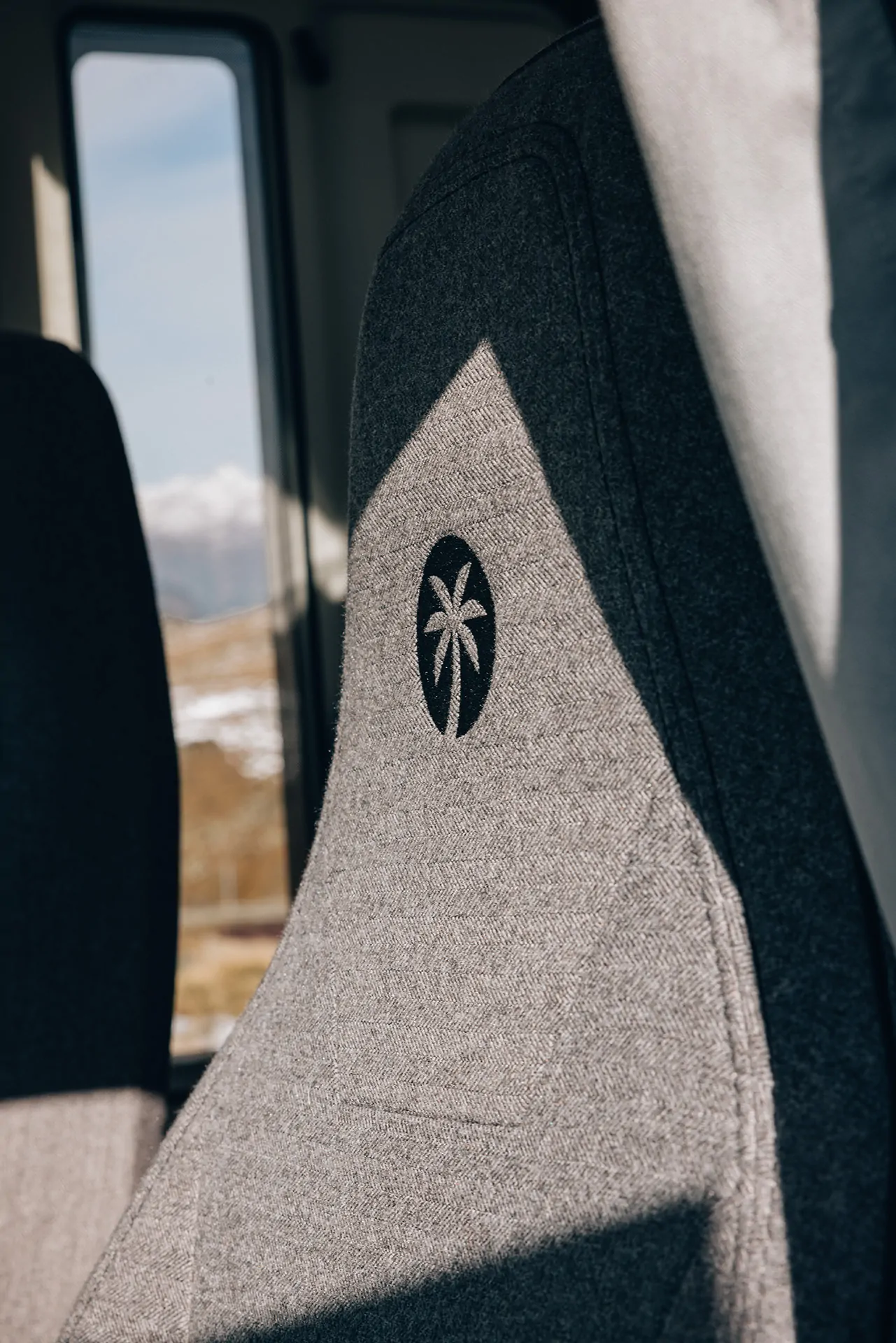 Grauer Autositz mit eingestickter Palme im Sonnenlicht.