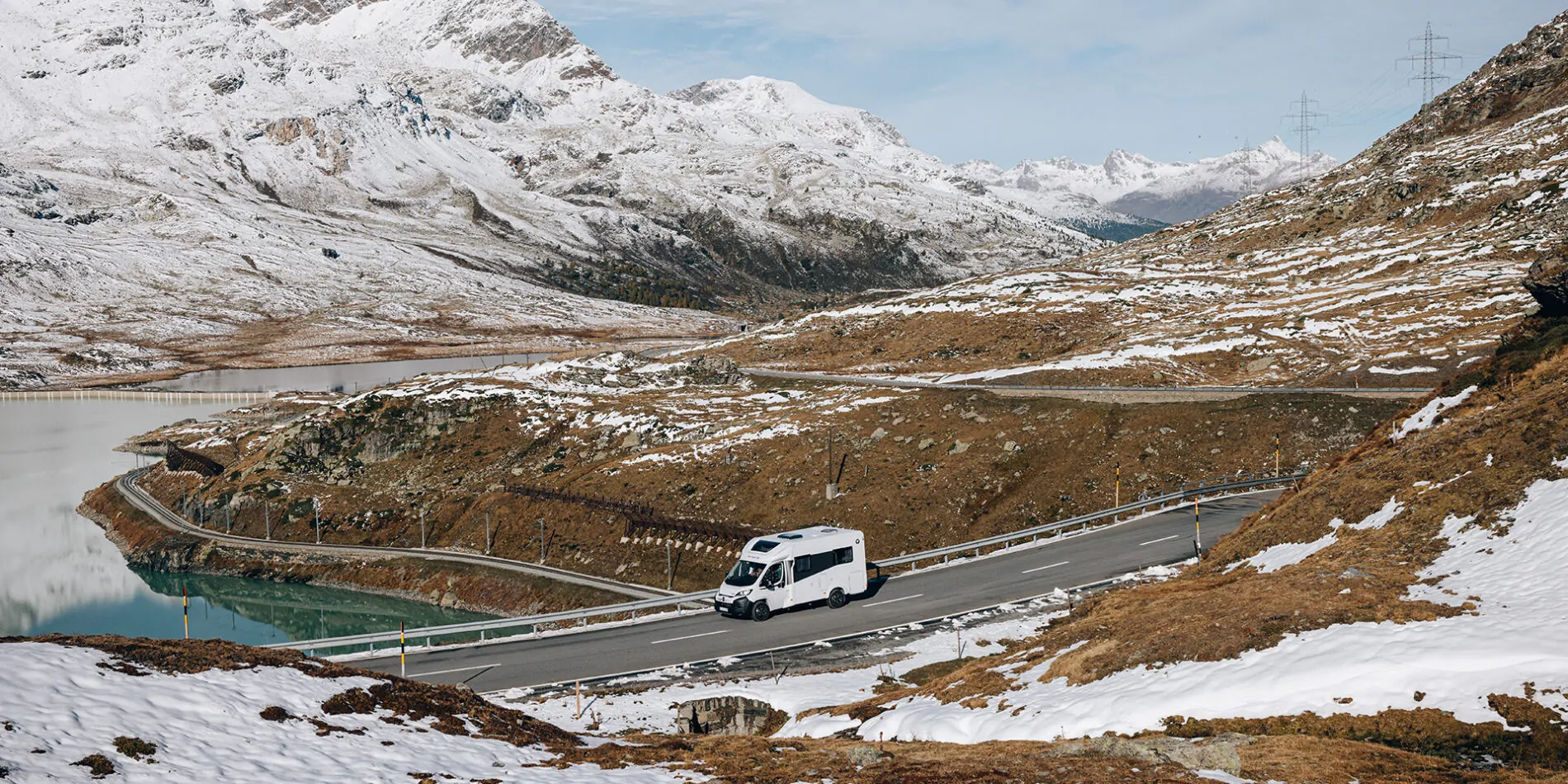 Ein teilintegriertes Wohnmobil fährt auf einer kurvigen Bergstraße in schneebedeckter Landschaft.