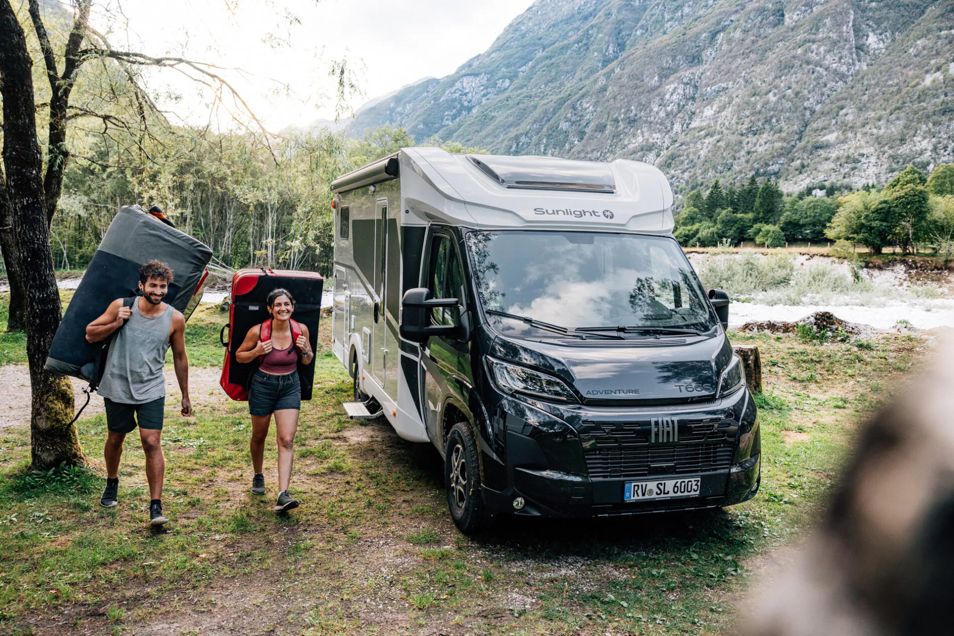 Zwei Personen tragen Kletterausrüstung neben einem Fiat Sunlight Wohnmobil.