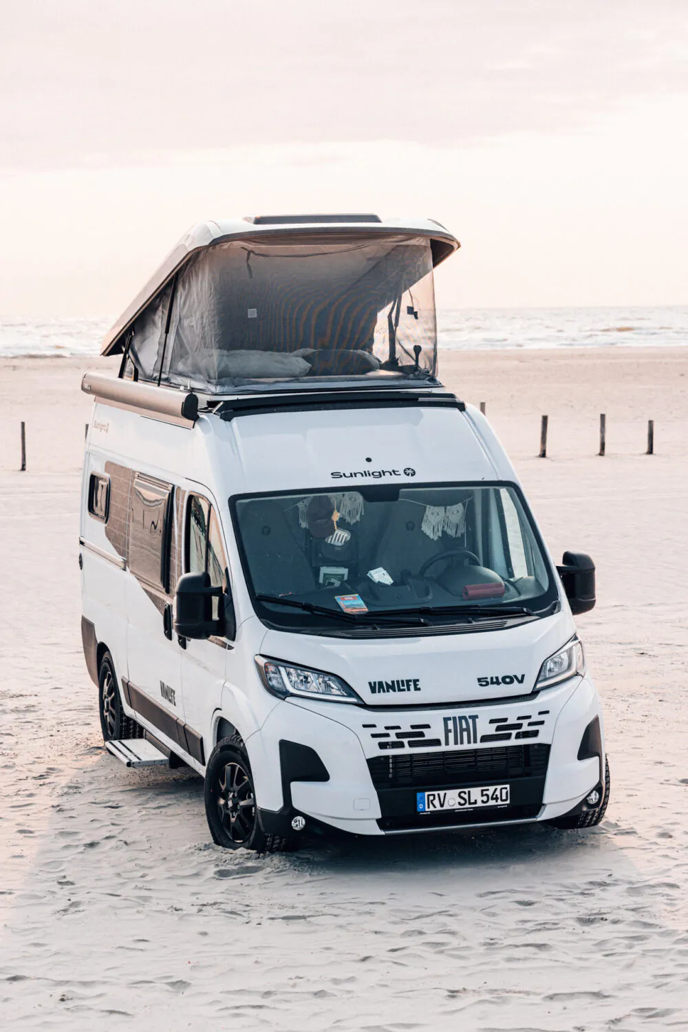 Ein Fiat Wohnmobil mit geöffnetem Aufstelldach steht am Strand.
