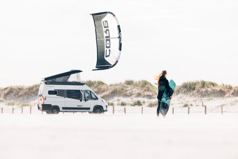 Kite-Surferin am Strand neben einem VanTourer Camper.
