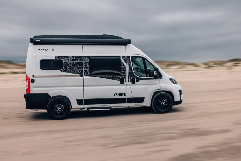 Ein weißer Sunlight Campervan fährt am Strand entlang.