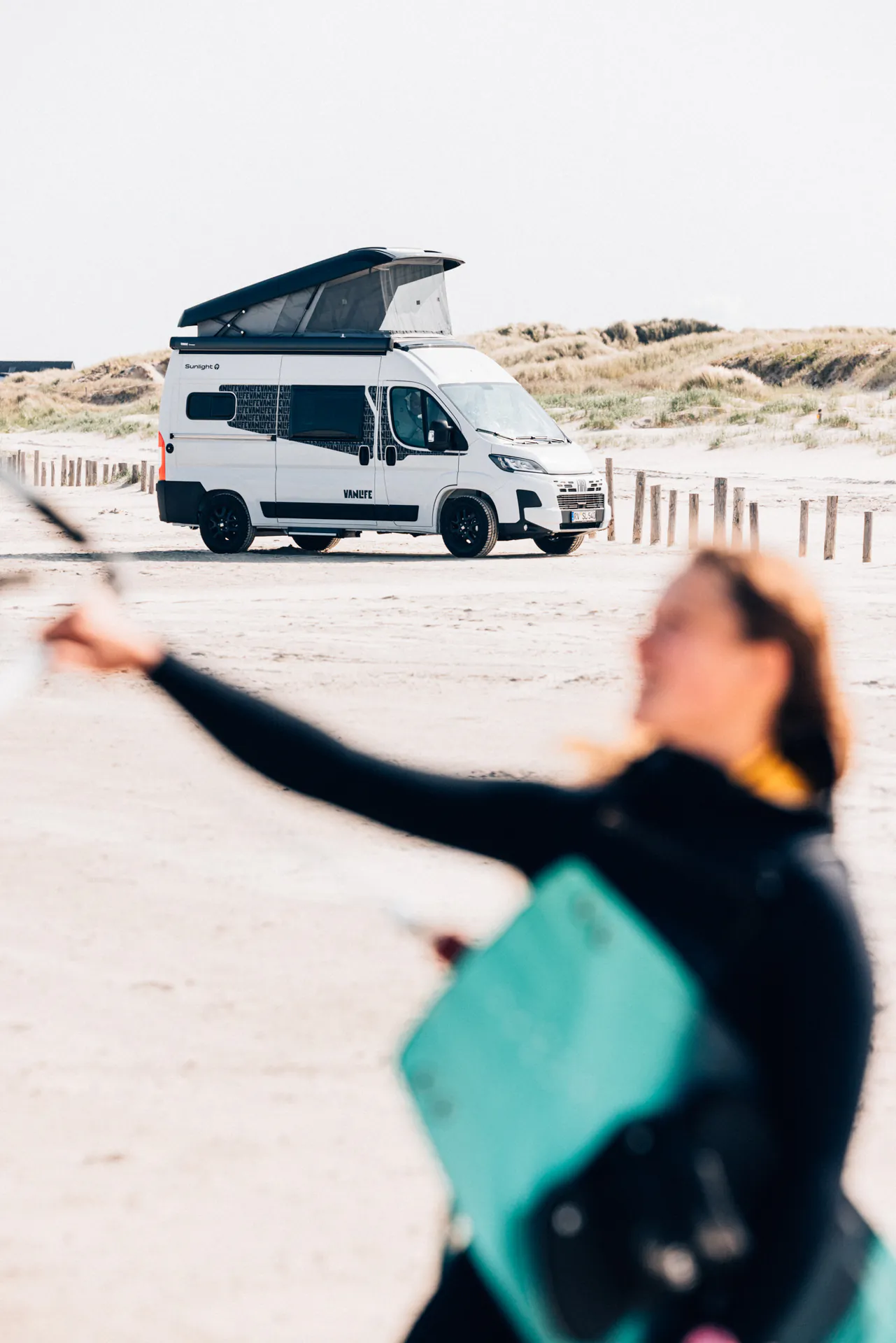 Weißer Sunlight Campervan mit geöffnetem Dach am Strand.