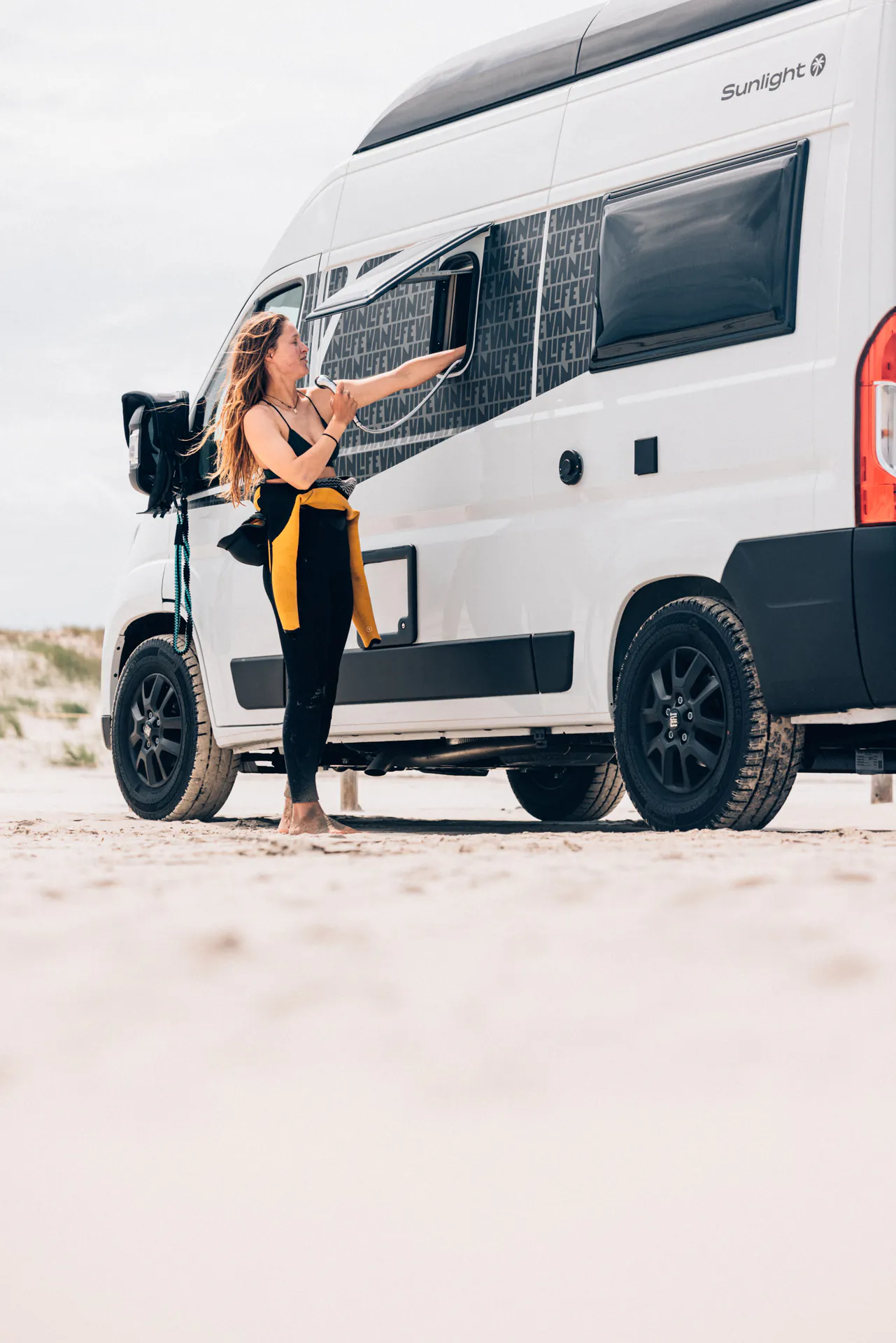 Frau öffnet das Fenster eines Sunlight-Campers am Strand.