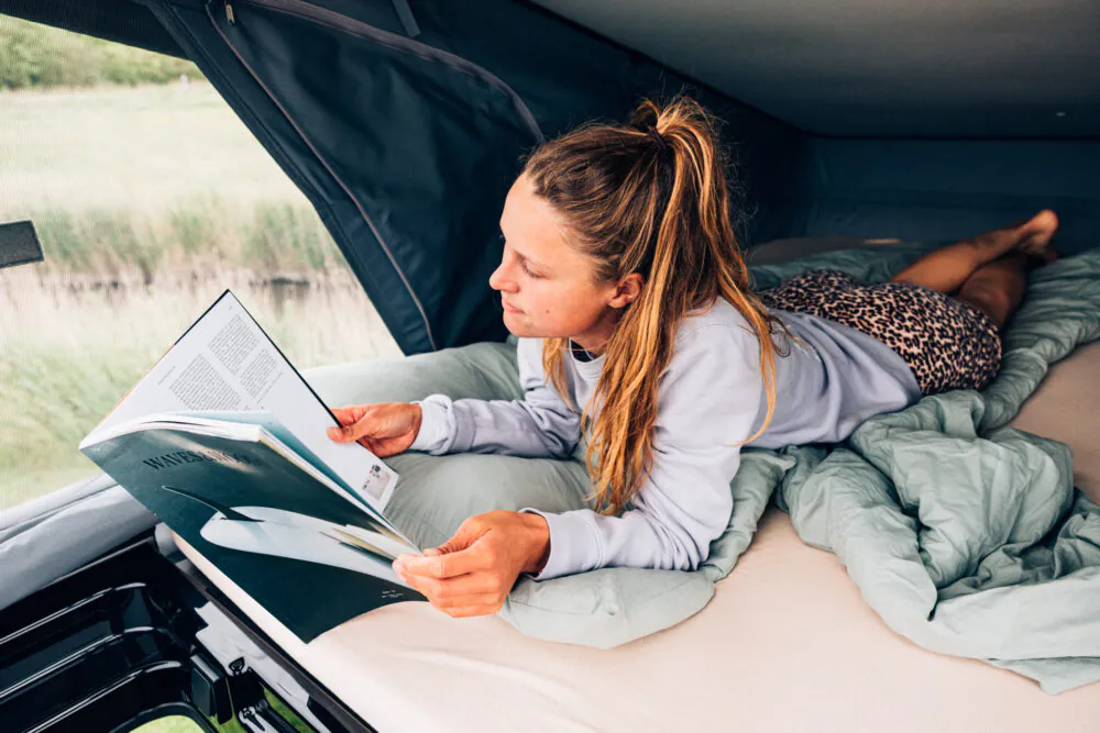 Eine Frau liest ein Buch, während sie auf einem Bett in einem Camper liegt.