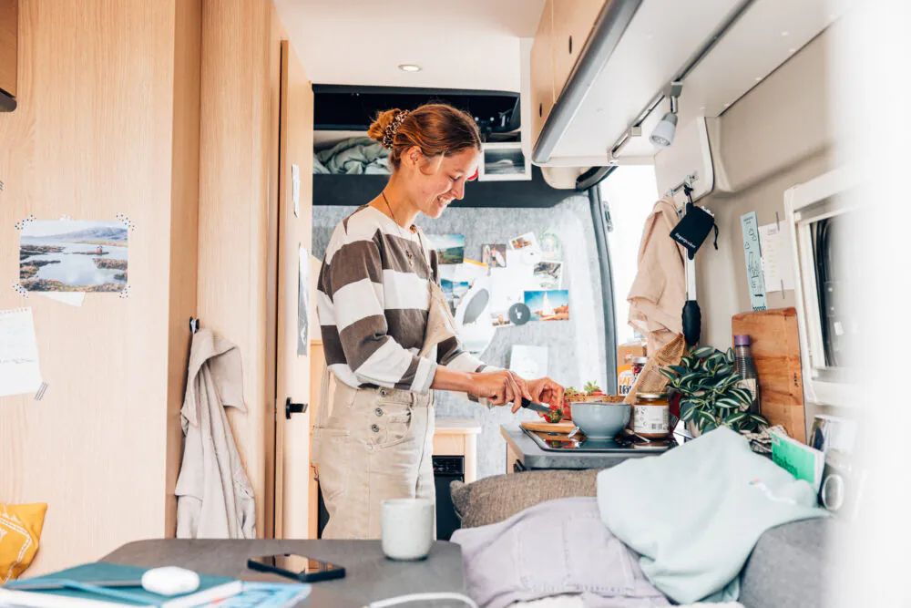 Eine Person bereitet in einem gemütlichen Van-Interieur eine Mahlzeit zu.