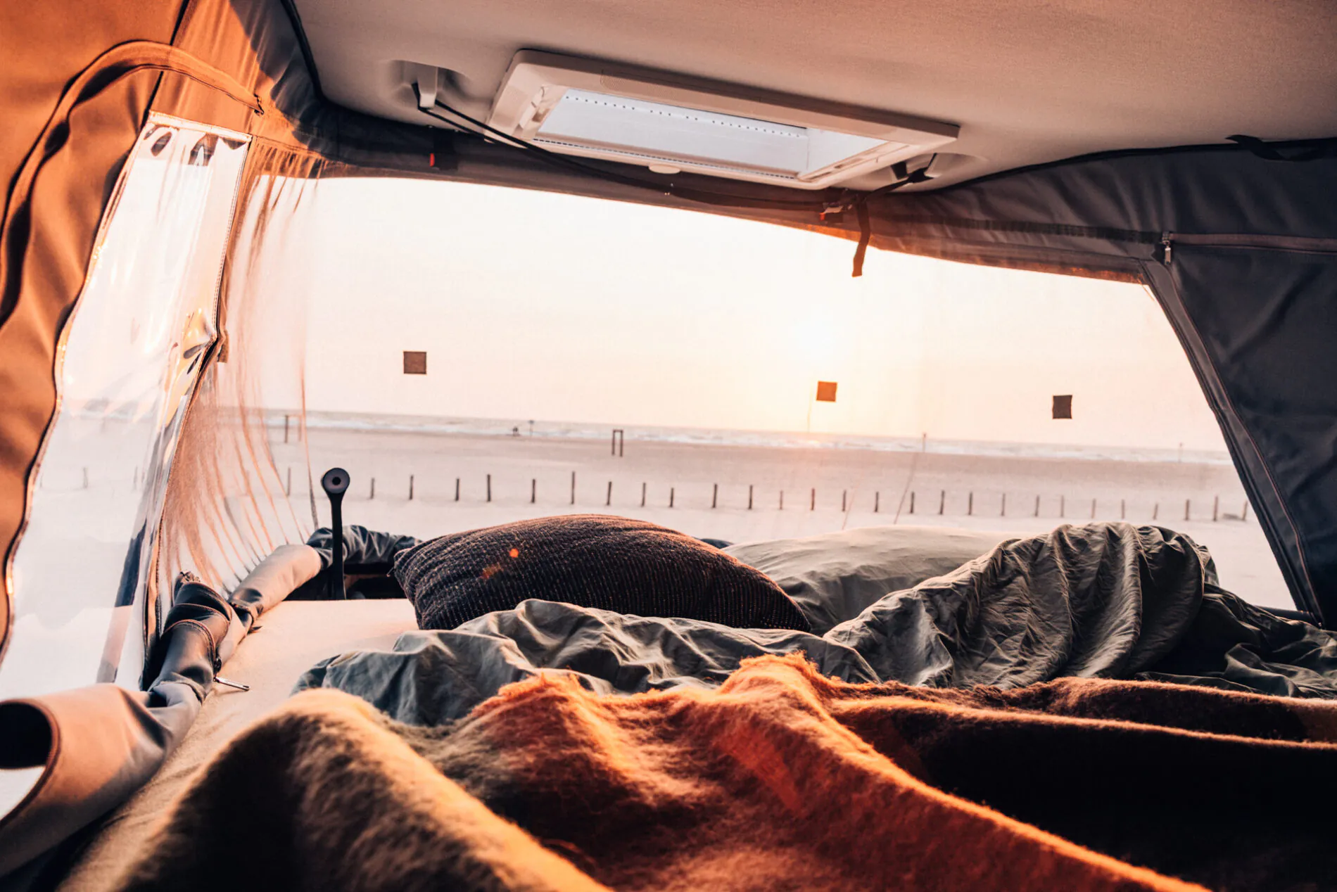 Blick aus dem Innenraum eines Campers auf einen Strand bei Sonnenuntergang.
