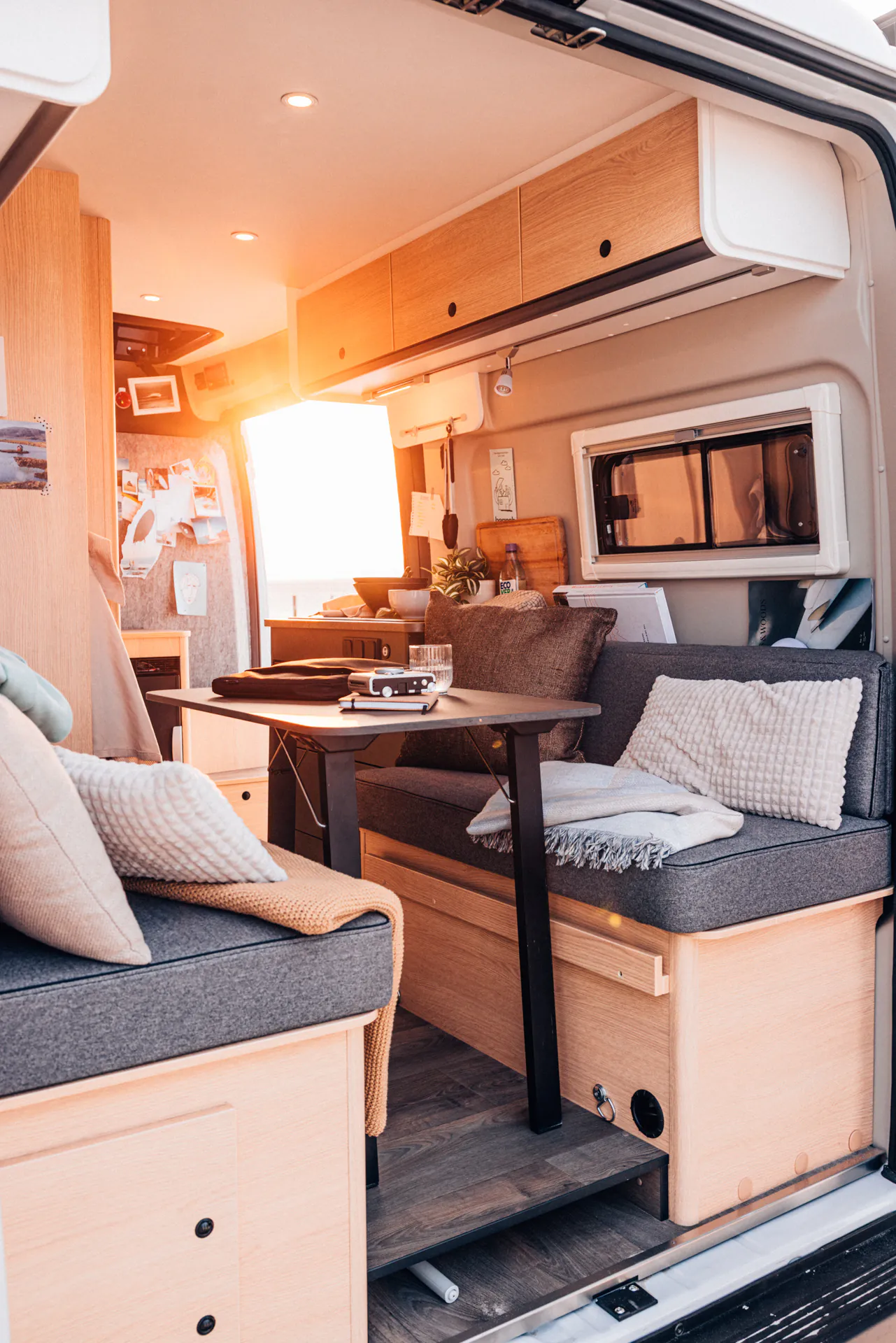 Innenansicht eines gemütlich eingerichteten Camper-Vans mit Sitzbank, Tisch und Dekoration.