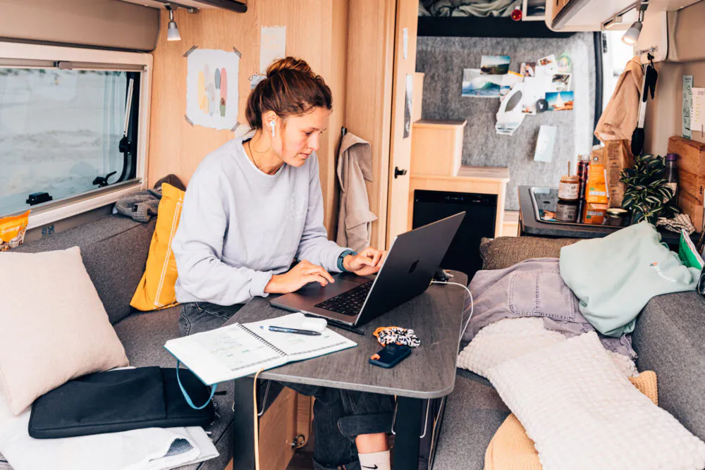 Person arbeitet an einem Laptop im gemütlichen Interieur eines Wohnmobils.