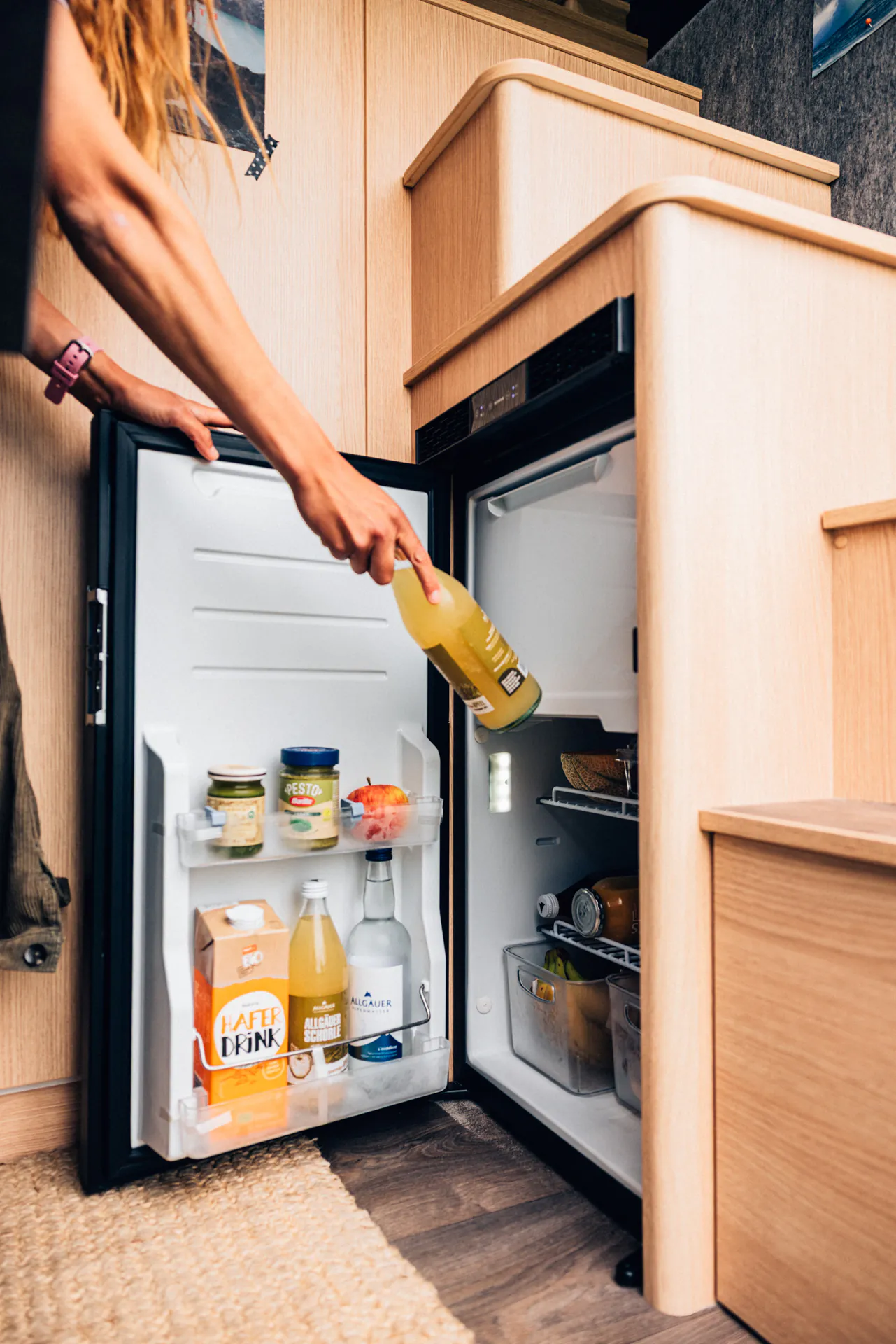 Person entnimmt eine Flasche aus einem offenen Kühlschrank in einem Camper.