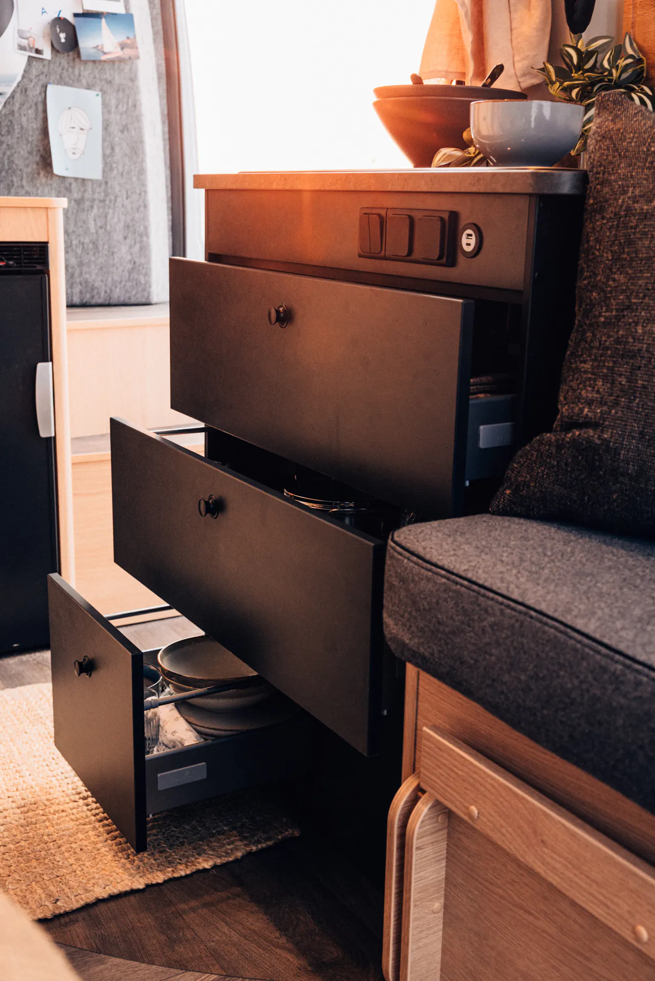 Innenansicht eines Campers mit geöffneten Küchenschubladen, gefüllt mit Geschirr.